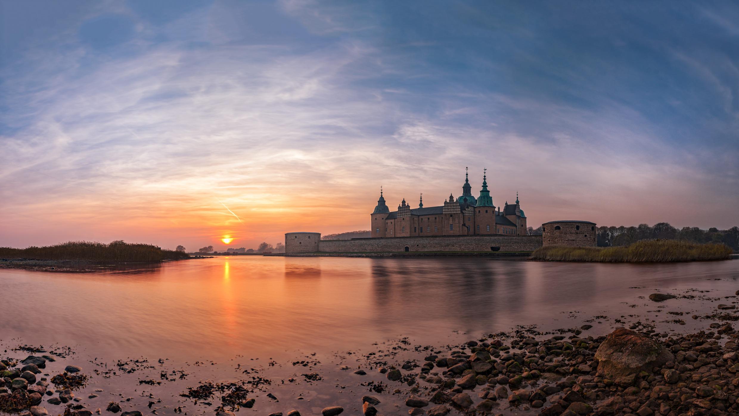 Ein Schloss am Wasser. Links davon geht die Sonne unter.