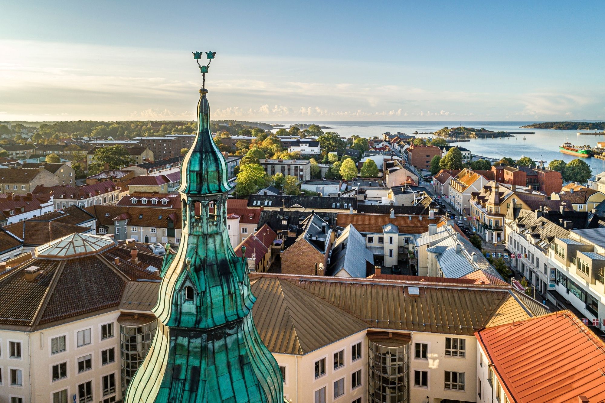 Luchtfoto van Karlshamn, met een groene koperen kerktoren die boven de kleurrijke daken uitsteekt en straten die naar de haven en de Oostzee leiden.
