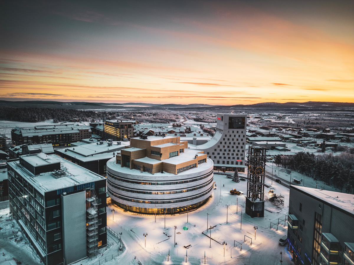 Het met sneeuw bedekte stadscentrum van Kiruna met moderne gebouwen en een klokkentoren, gezien bij zonsondergang in de winter.