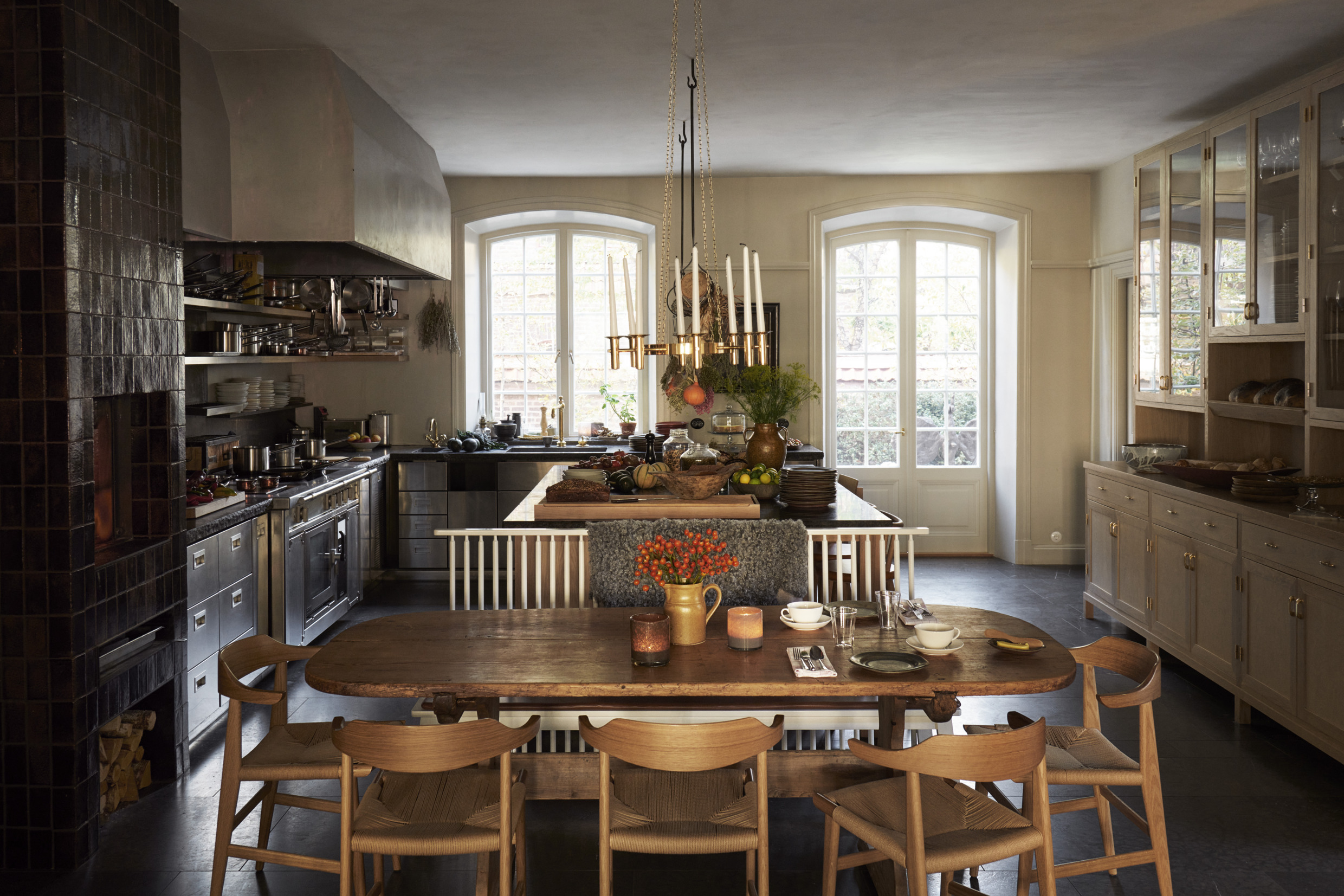 A light coloured wooden table in front of a kitchen island filled with different types of food.