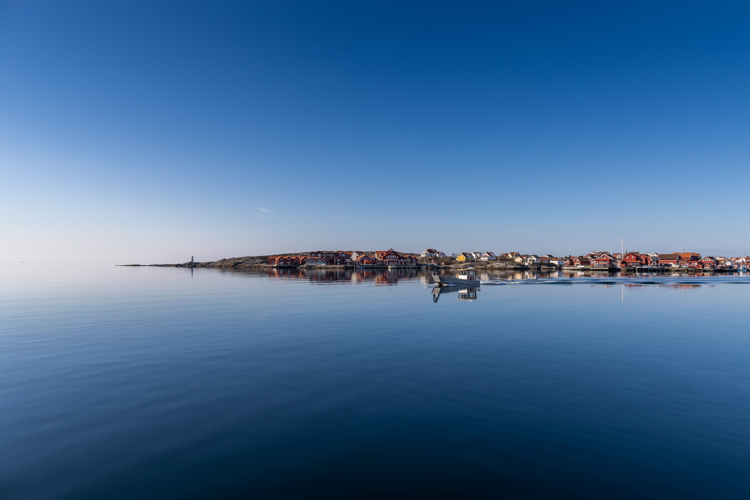 An island in the archipelago with red wooden houses and a white boat in the foreground under clear blue skies.