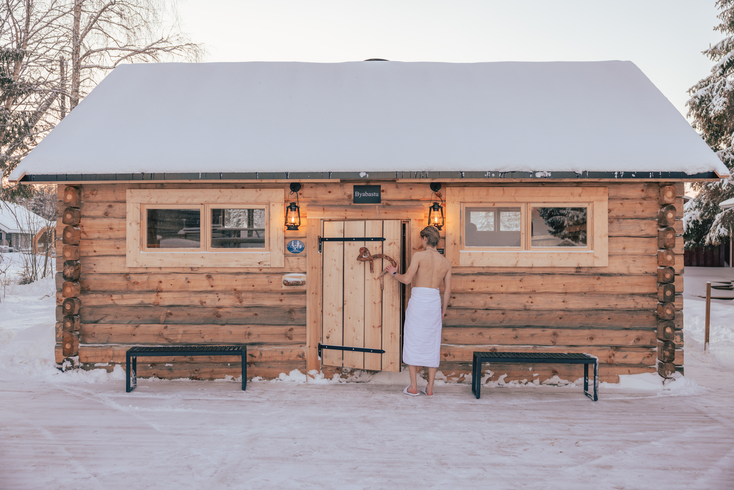 A person with a white towel is entering a wooden hut.