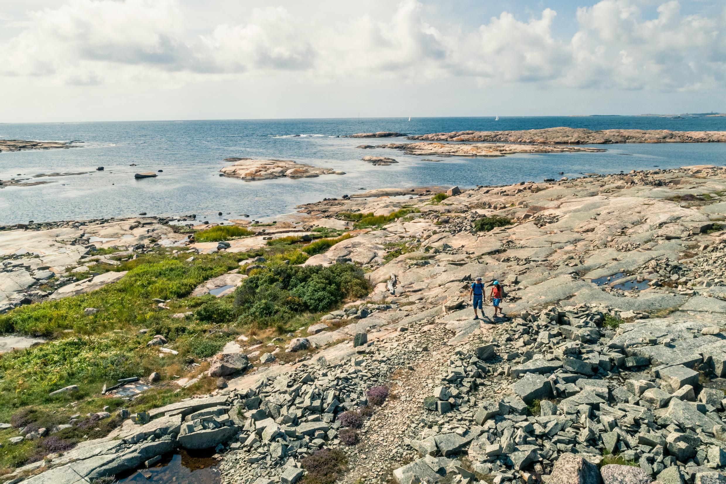 A couple with backpacks are hiking on a trail on the cliffs along the coast.