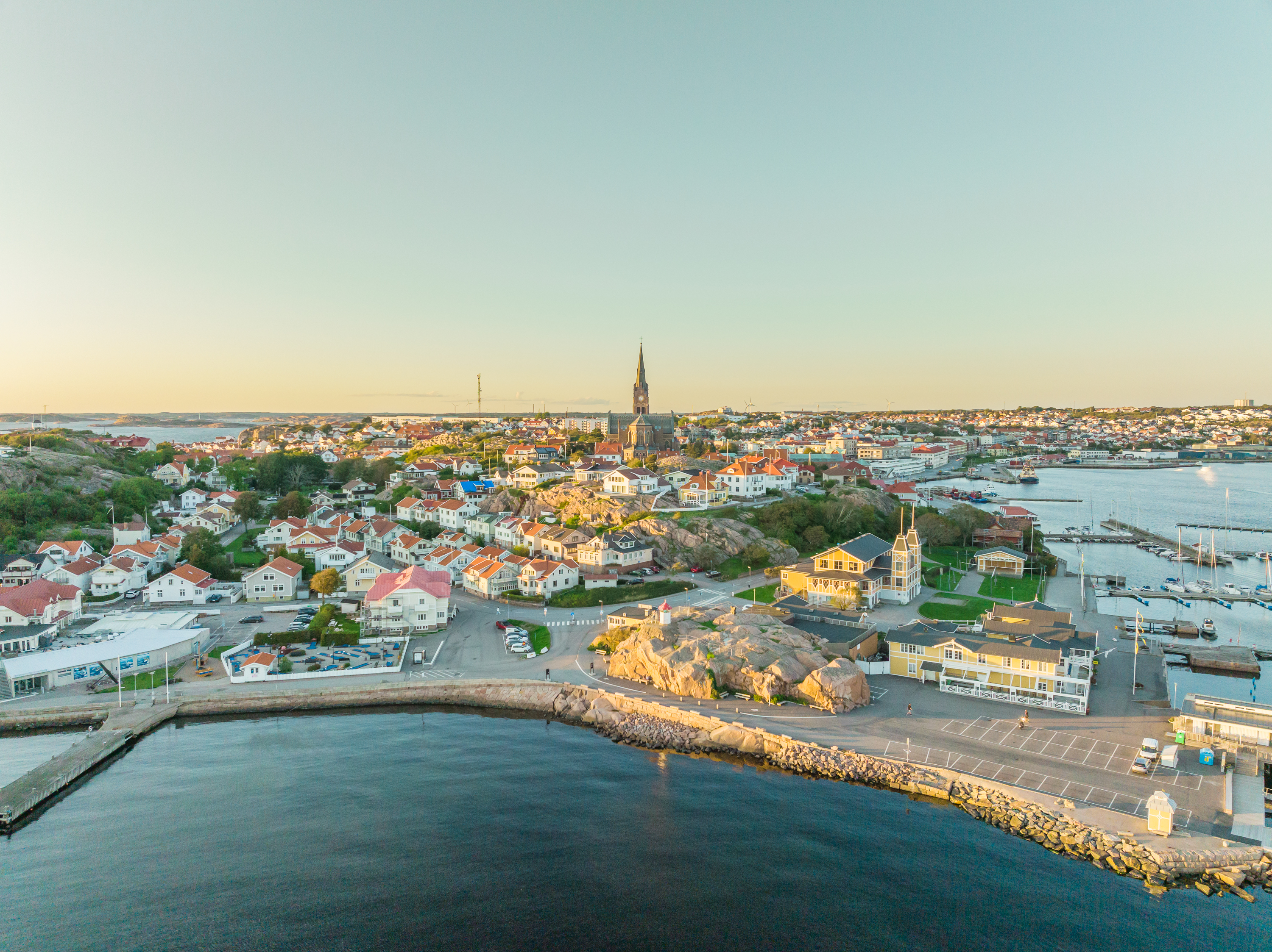 Luchtfoto van Lysekil met huizen aan de kust, een kerktoren, de haven en de omringende zee in het avondlicht.