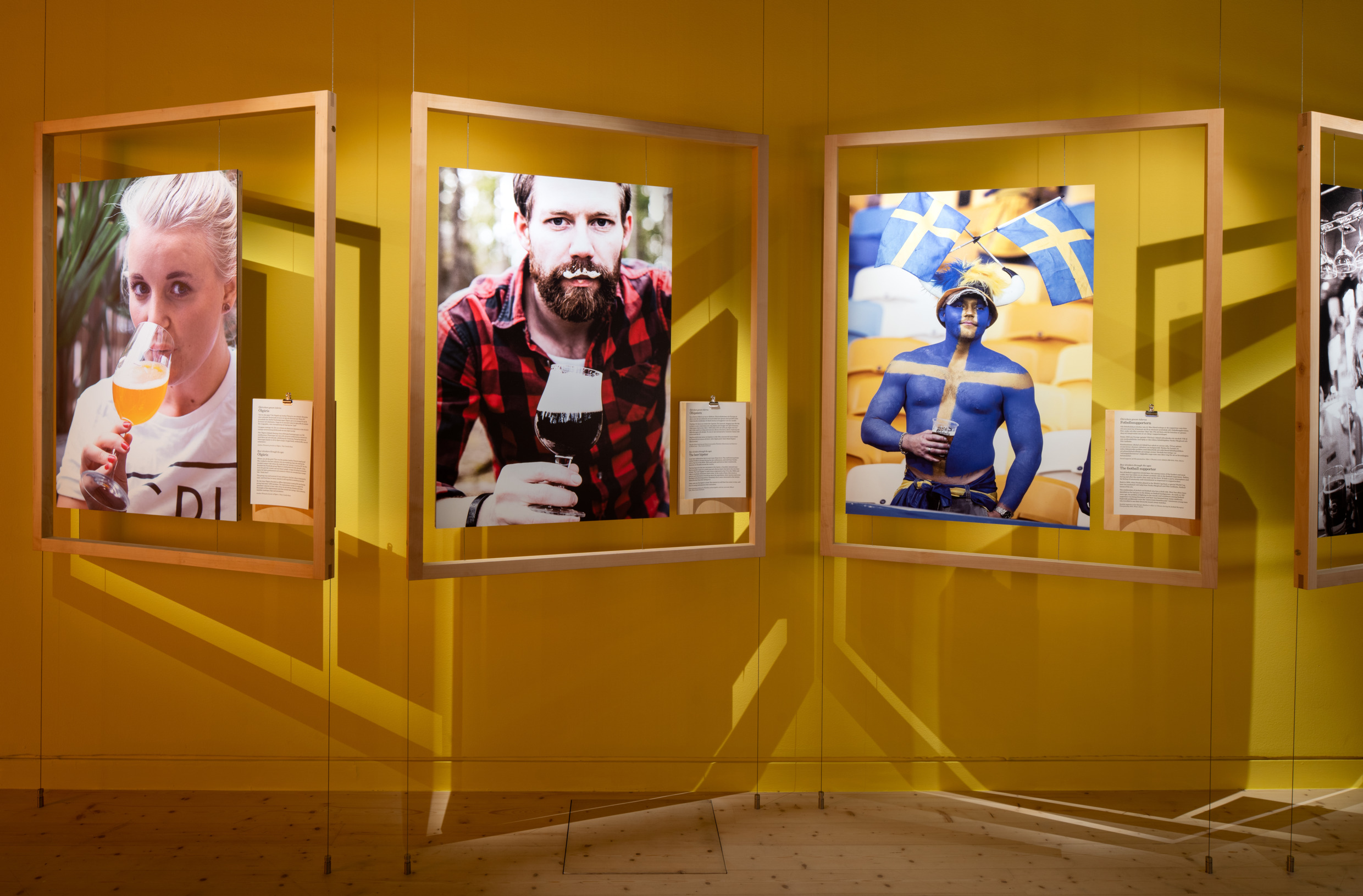 Pictures in wooden frames of men and women drinking various beverages as part of an exhibition.