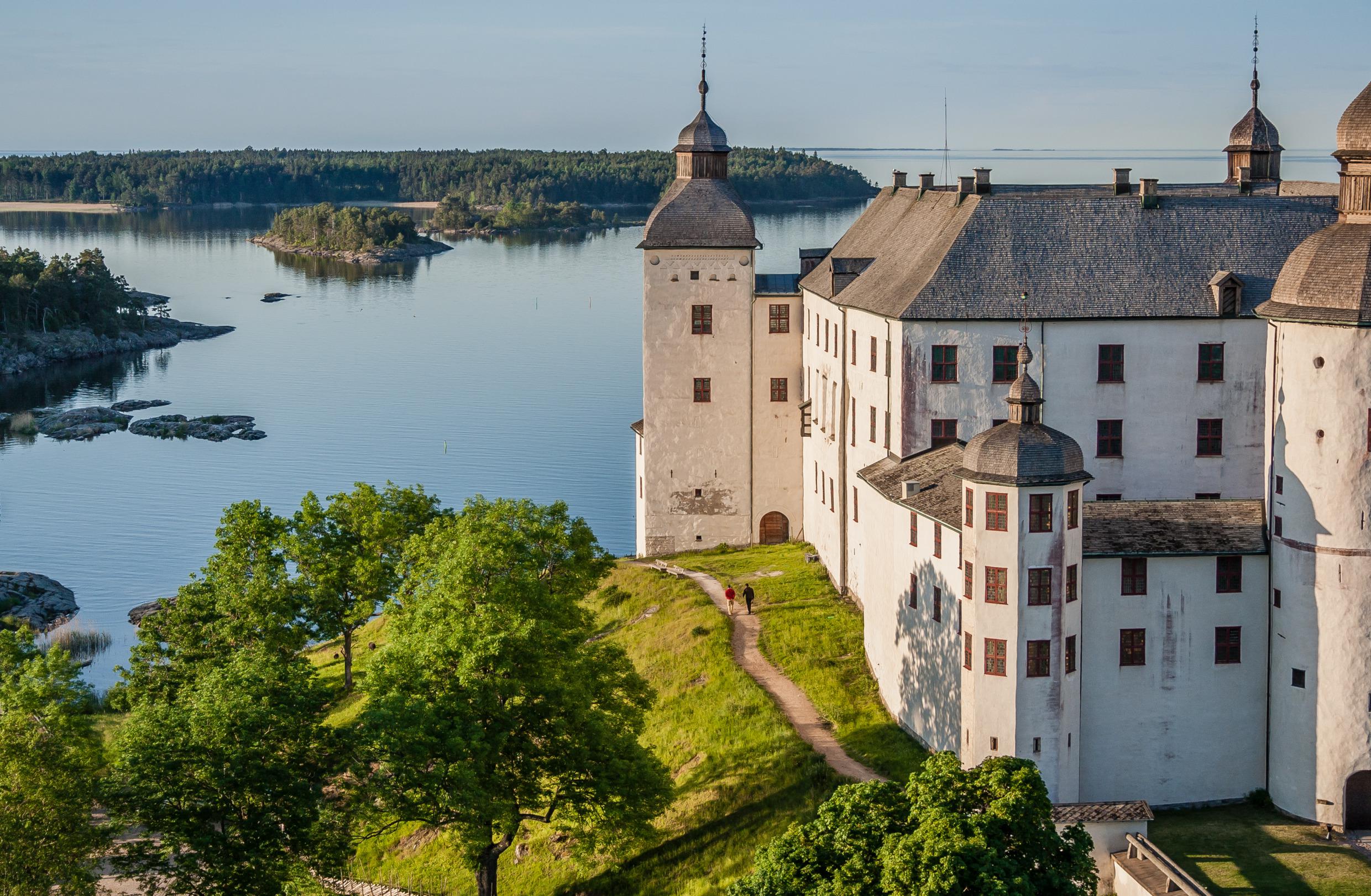 Läckö Castle on a green hill with Lake Vänern and a tree-filled island in the background.