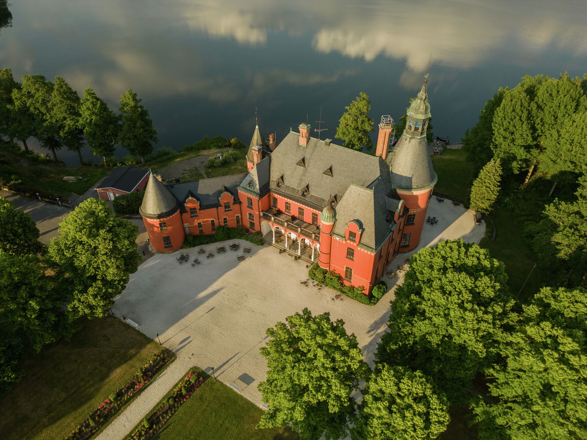 Vue aérienne du château de Lejondal, un château rouge situé au bord d'un lac, entouré d'arbres et surplombant le lac de Lejondal, près de Stockholm.