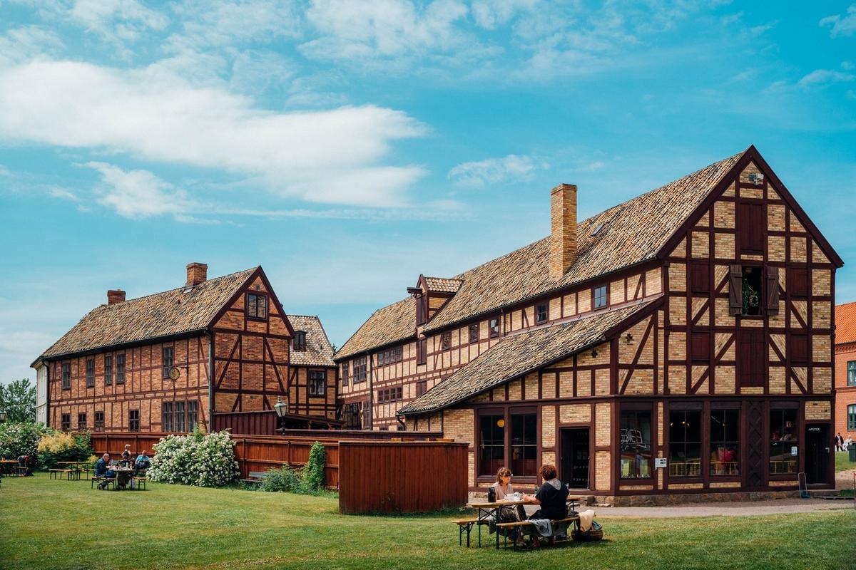 Historische Fachwerkgebäude und Besucher, die die Gärten des Freilichtmuseums Fredriksdal in Helsingborg genießen.