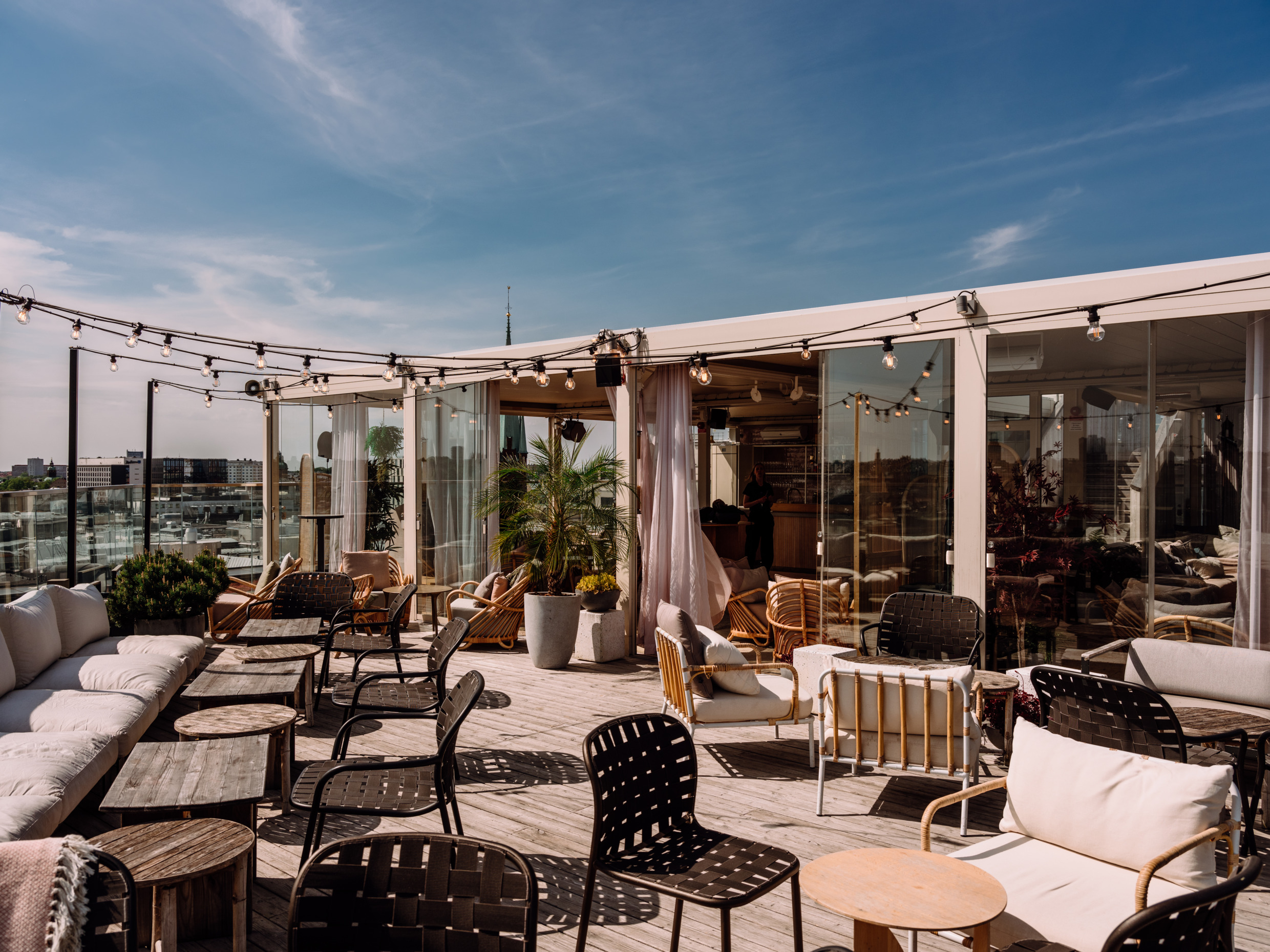 Rooftop terrace at TAK in Stockholm, with lounge seating, string lights and views over the city – set up for dinner and drinks in the sun.