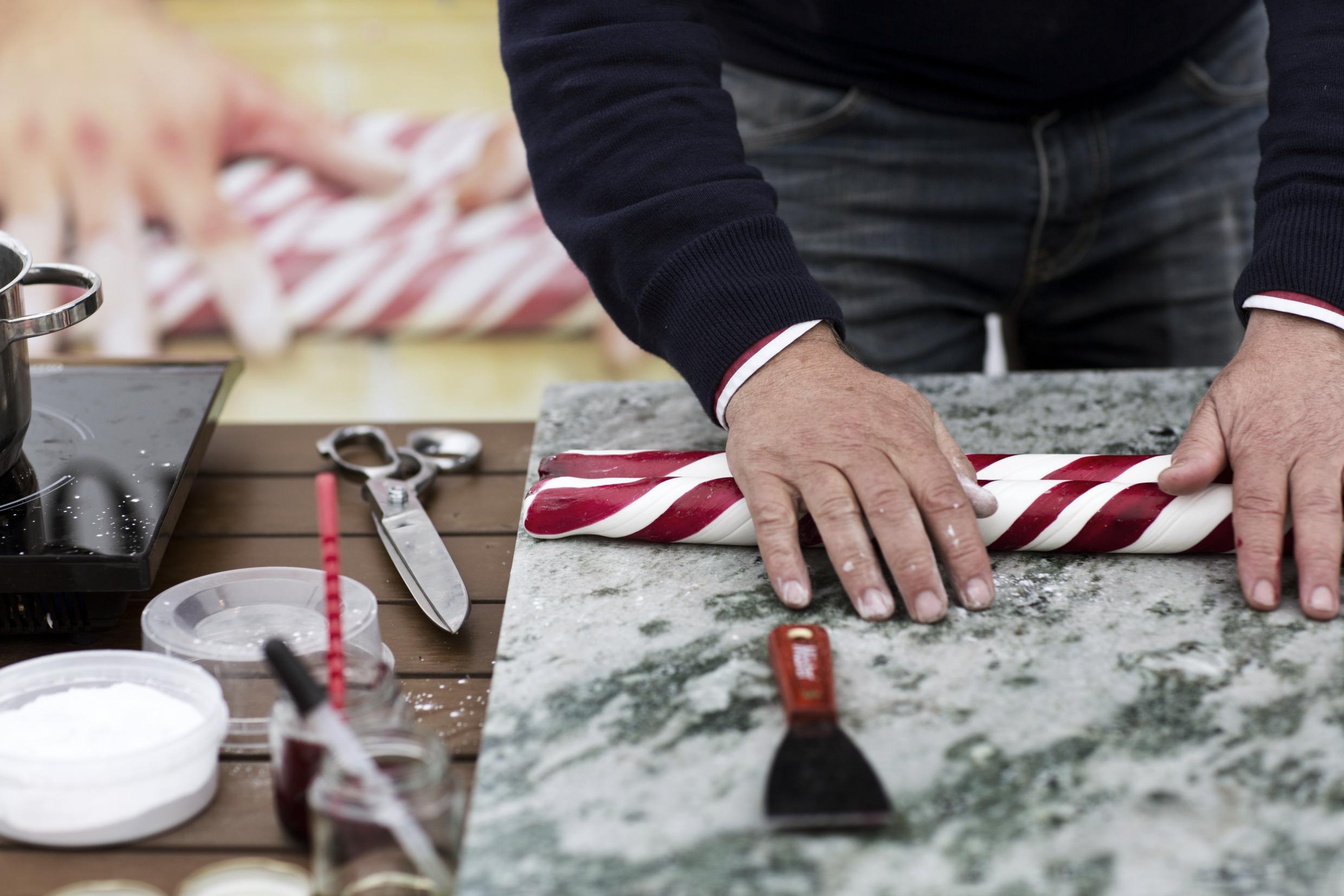 Een persoon is wit-rode zuurstokken aan het rollen. Zijn werkmateriaal ligt op tafel.