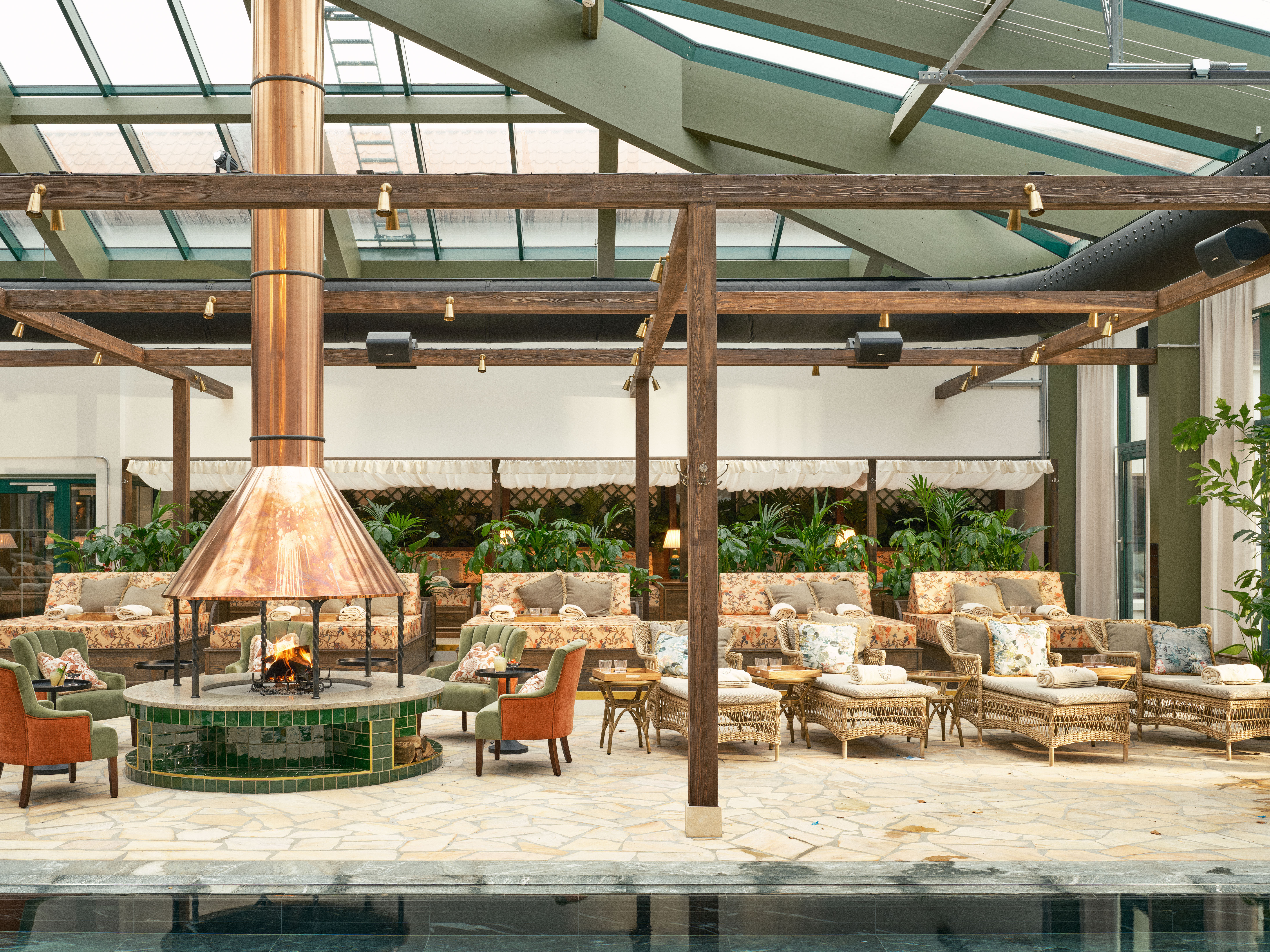 Le salon spa du Maryhill Estate, avec sa cheminée centrale, ses chaises longues confortables, ses plantes d'intérieur et son toit vitré baigné de lumière.