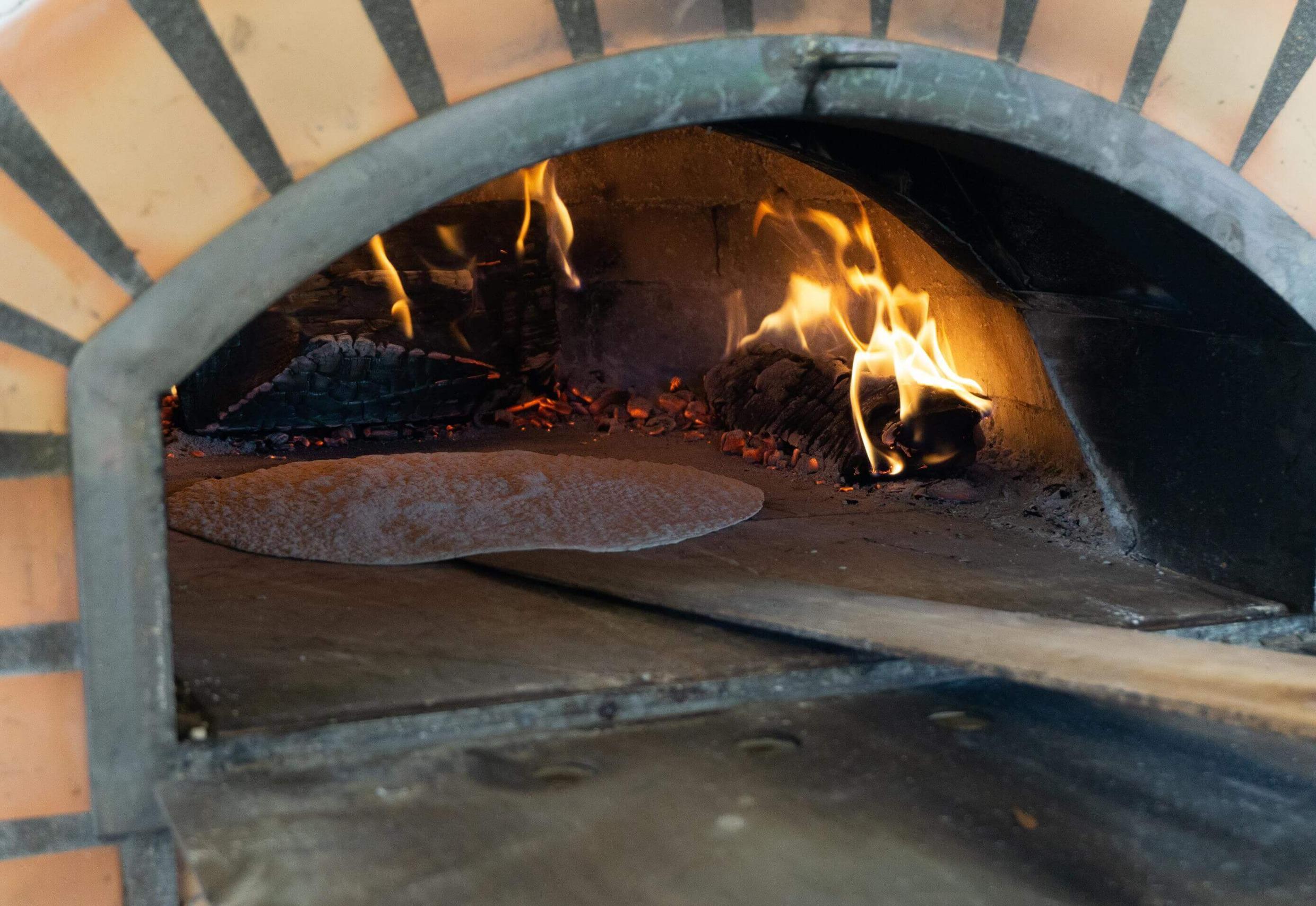Ein Fladenbrot wird in einen Holzofen gelegt.