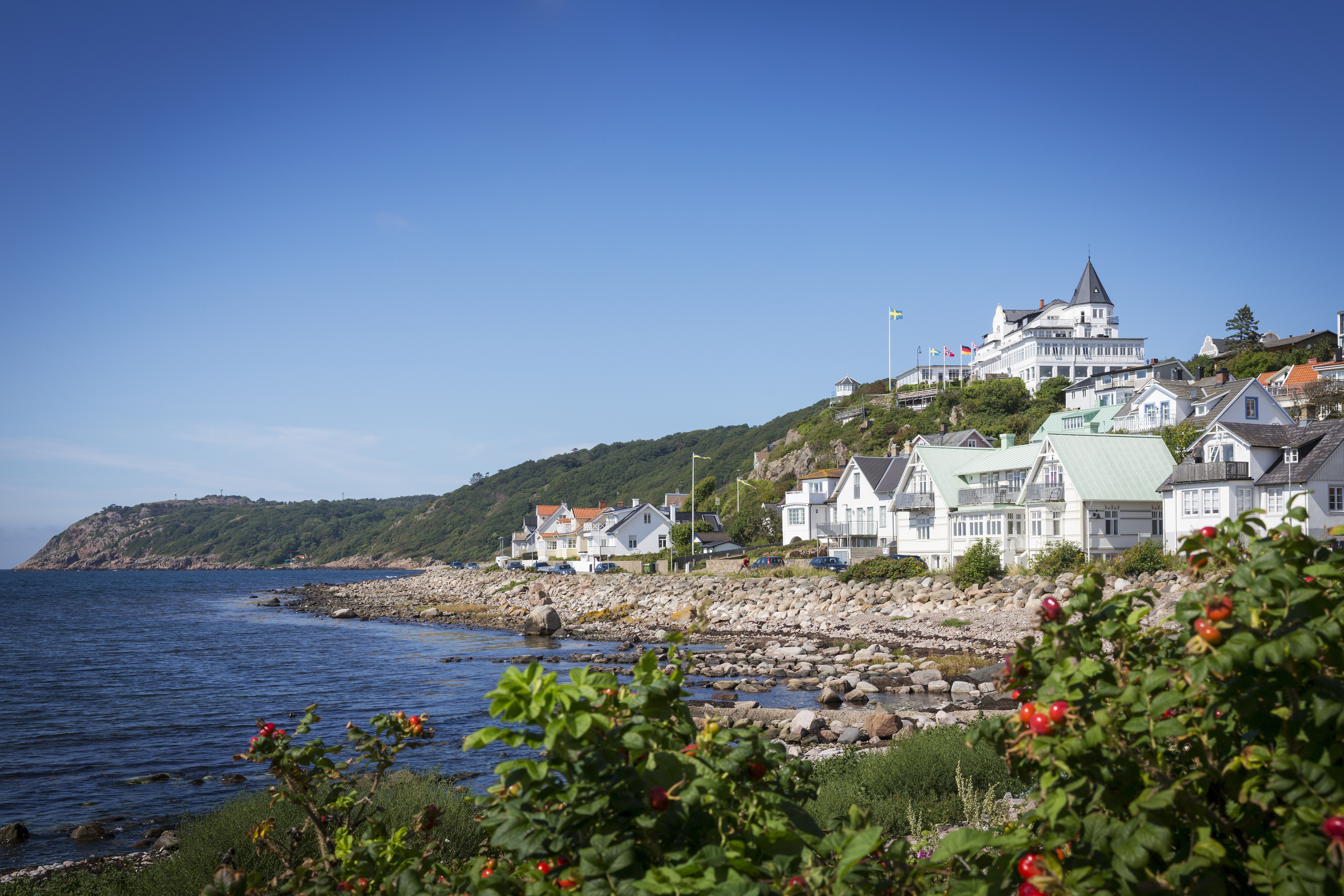 Uitzicht op de kust bij Mölle, met witte huisjes langs de rotsachtige kustlijn en het Grand Hotel Mölle dat vanaf de heuvel uitkijkt over de zee.