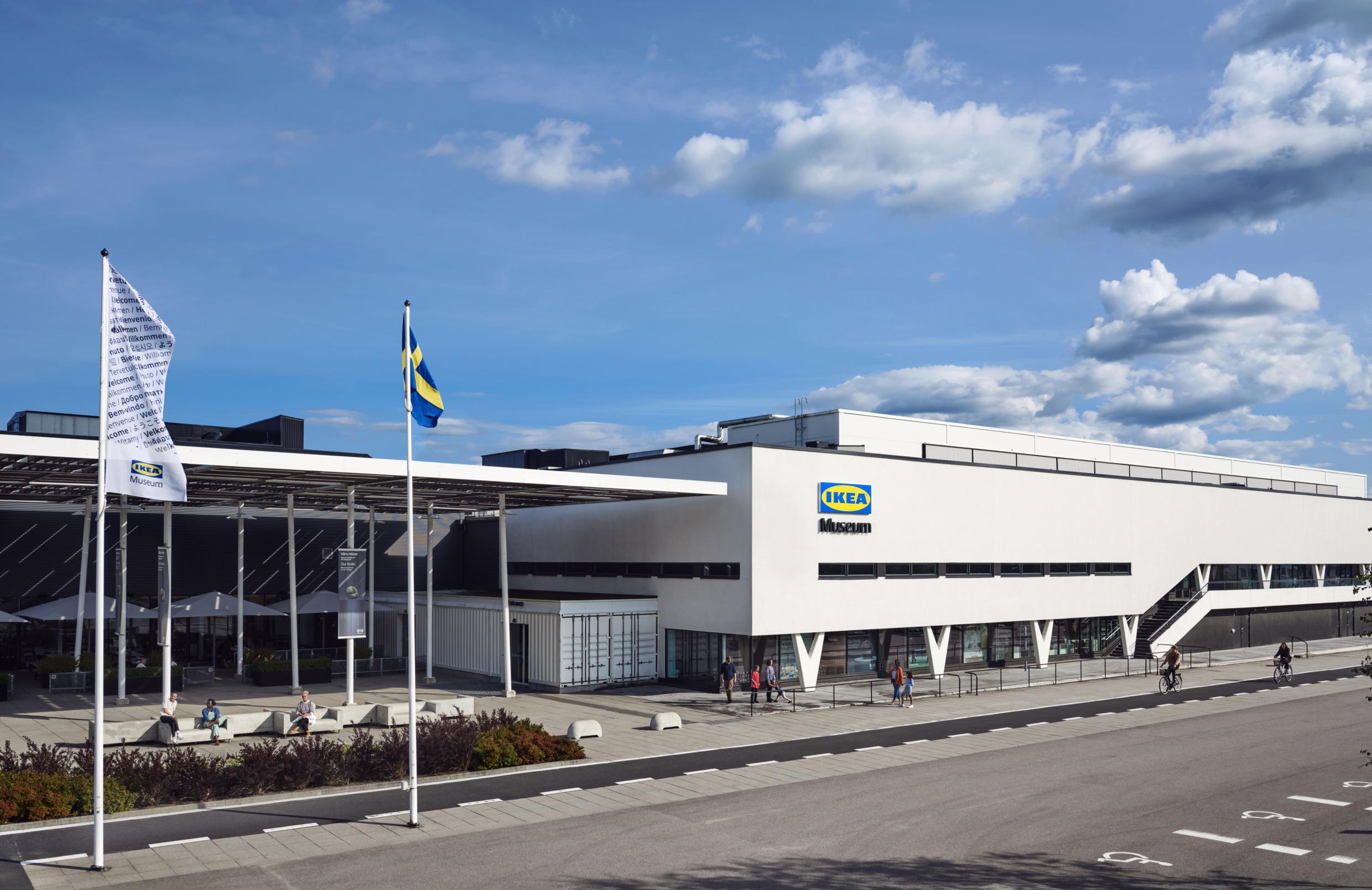 Un grand bâtiment blanc avec l'enseigne du musée IKEA sur le mur. Plusieurs personnes marchant devant le bâtiment.