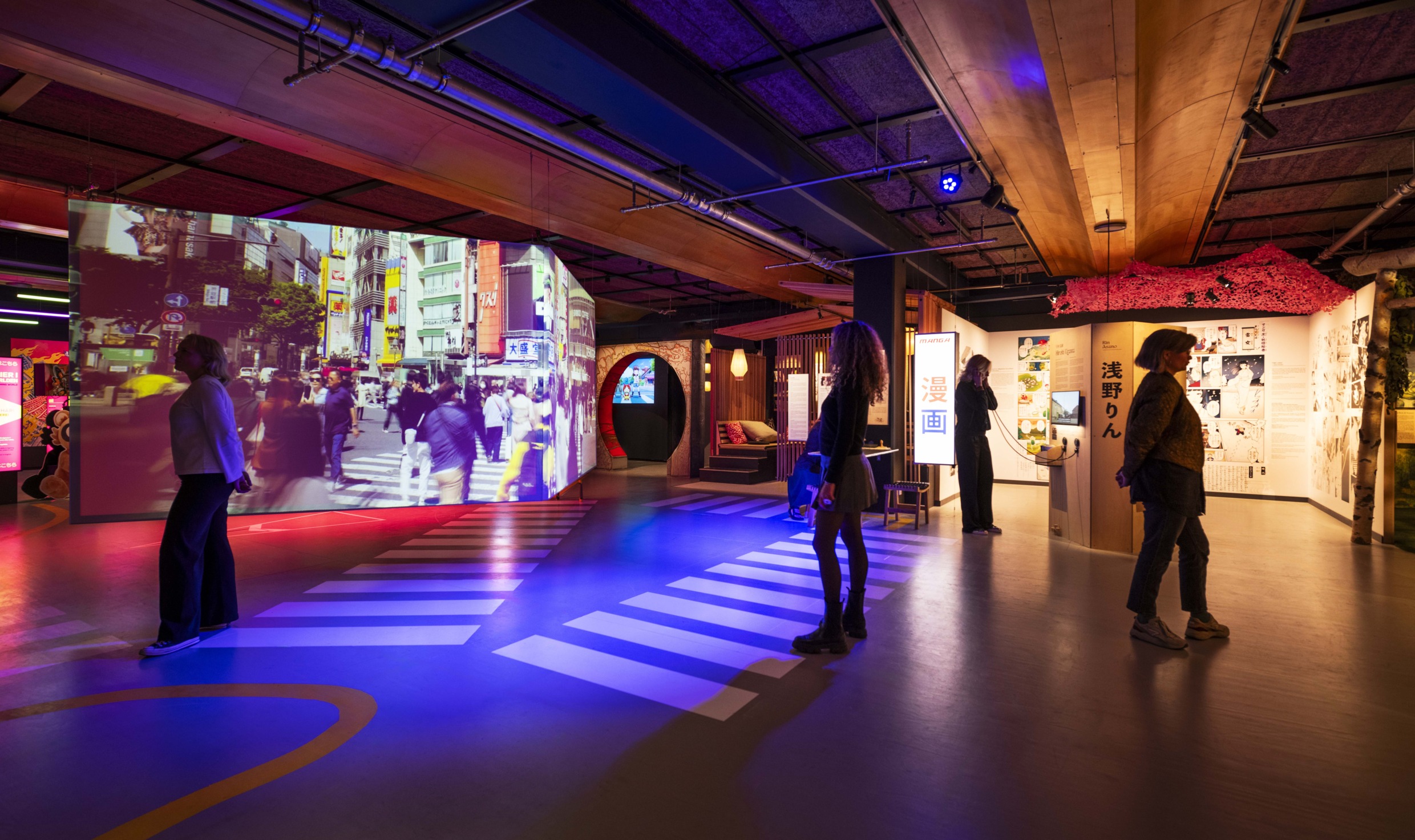 Mensen die een tentoonstelling bekijken in het Etnografisch Museum in Stockholm, met kleurrijke displays en een grote videoprojectie van een druk kruispunt in Tokio.