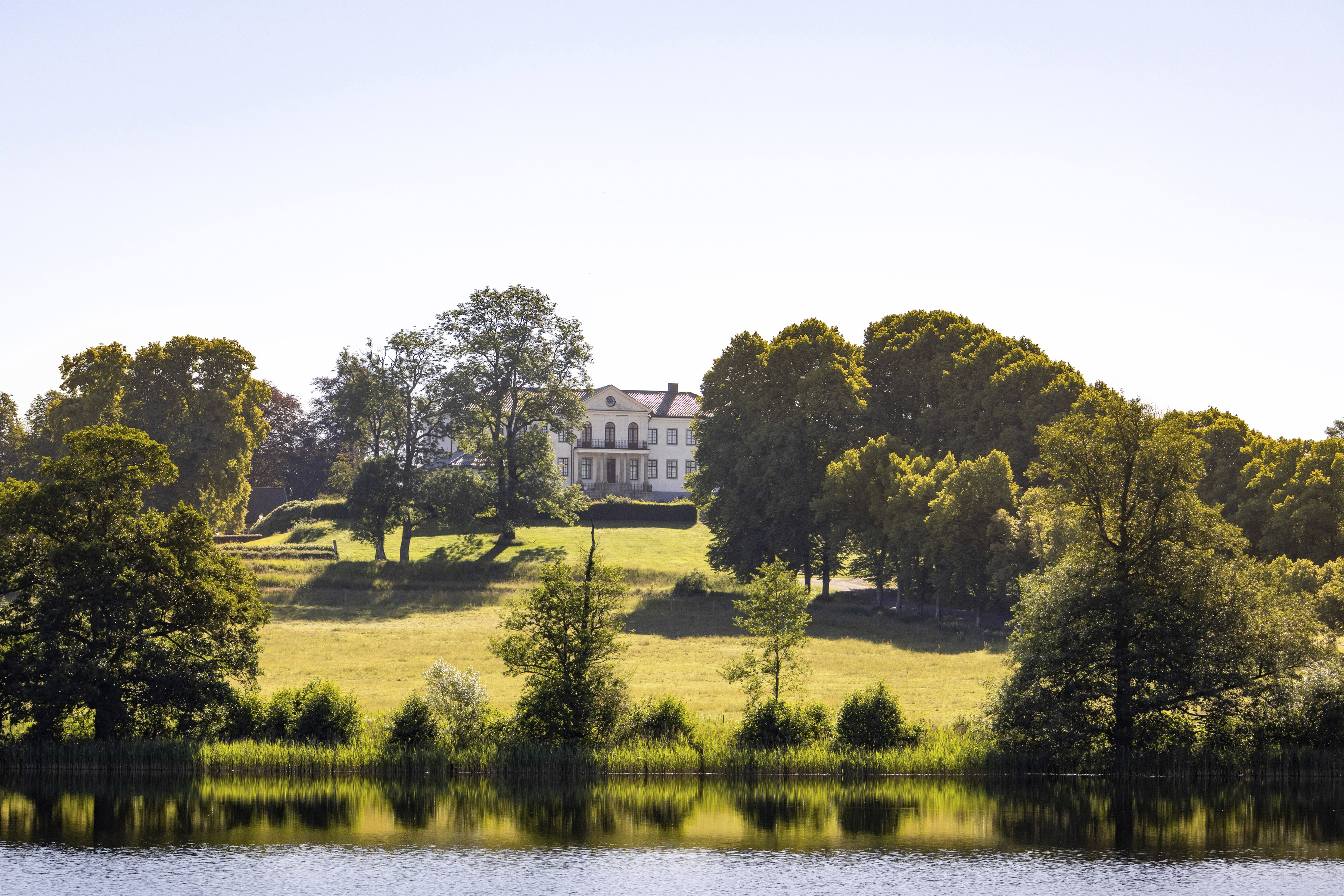Le château de Nääs, un manoir blanc surplombant un lac, entouré d'arbres et d'une campagne vallonnée, situé entre Göteborg et Alingsås.