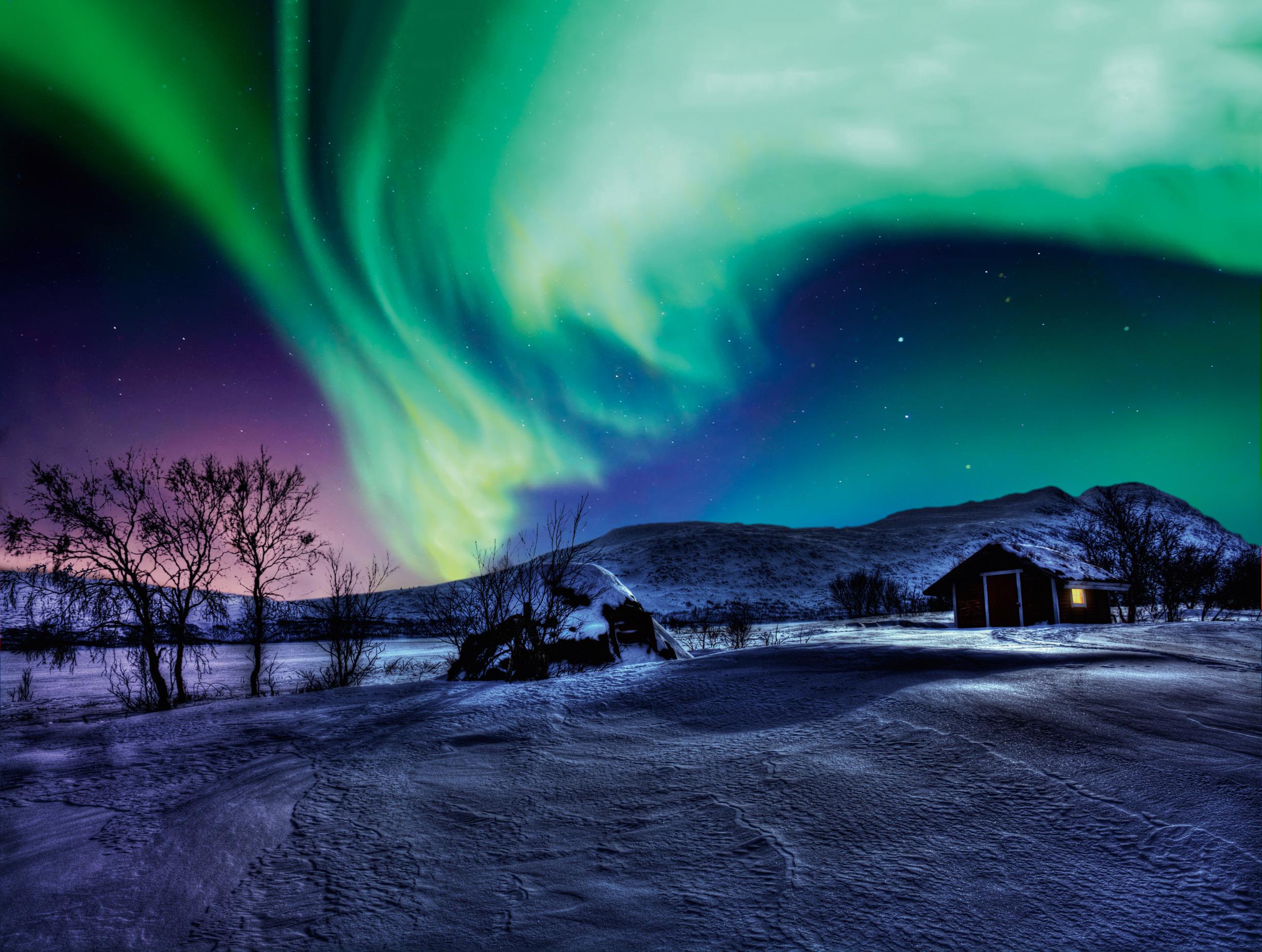 Das Nordlicht ist am Himmel über einer kleinen Hütte in den Bergen zu sehen.