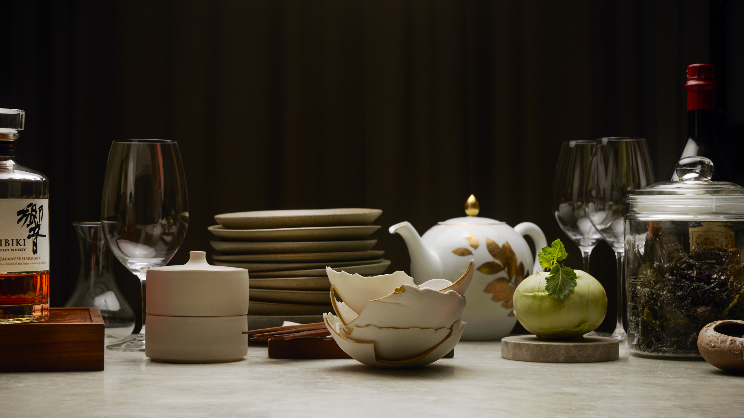 Een verfijnde tafelsetting in Nour, een restaurant met een Michelin-ster, met handgemaakt keramiek, glaswerk en ingrediënten die de fusie van Scandinavische en Japanse culinaire tradities weerspiegelen.