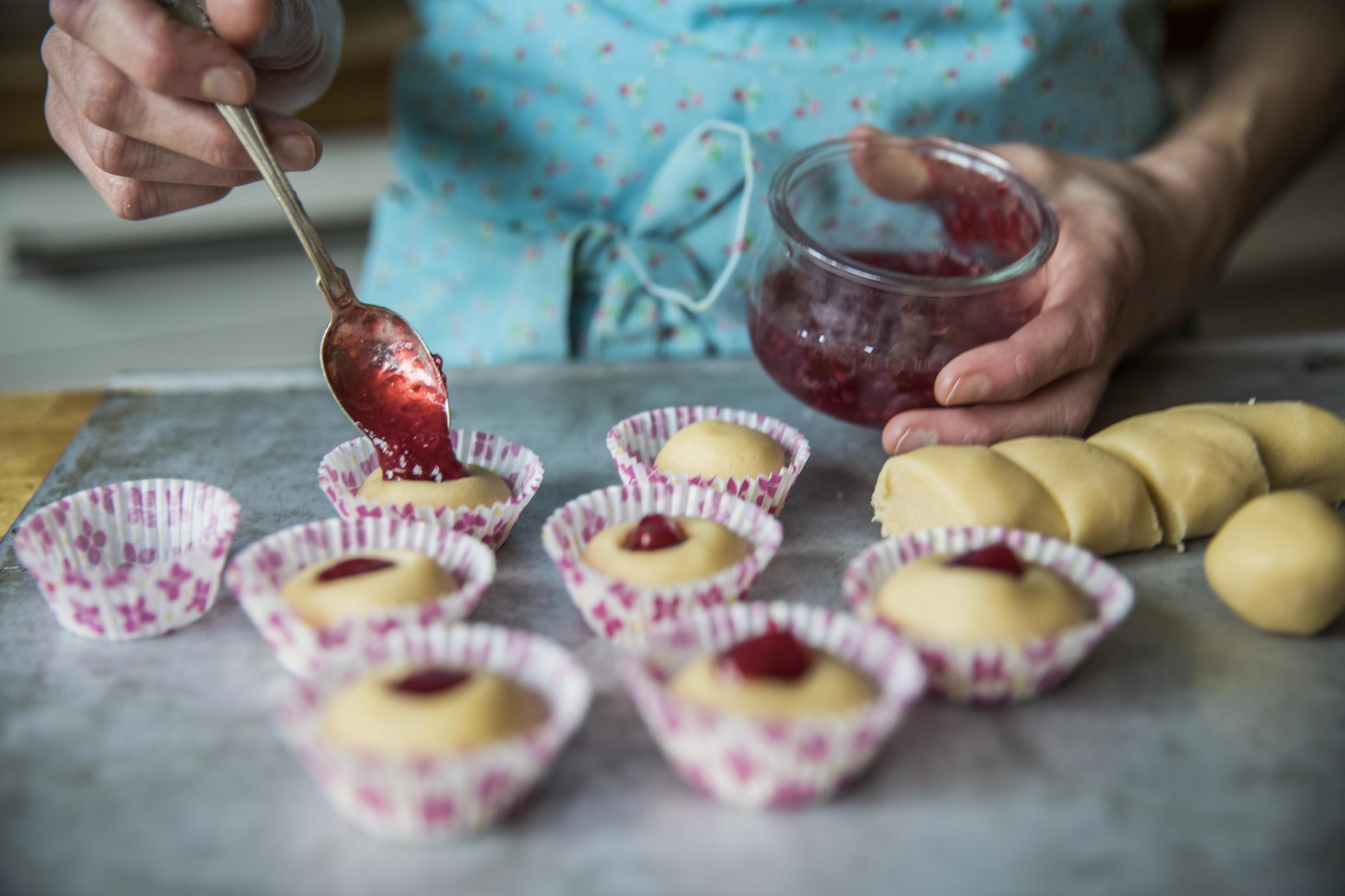 Une personne est en trian de mettre de la confirture dans des biscuits pour en faire des grottes à la framboise.