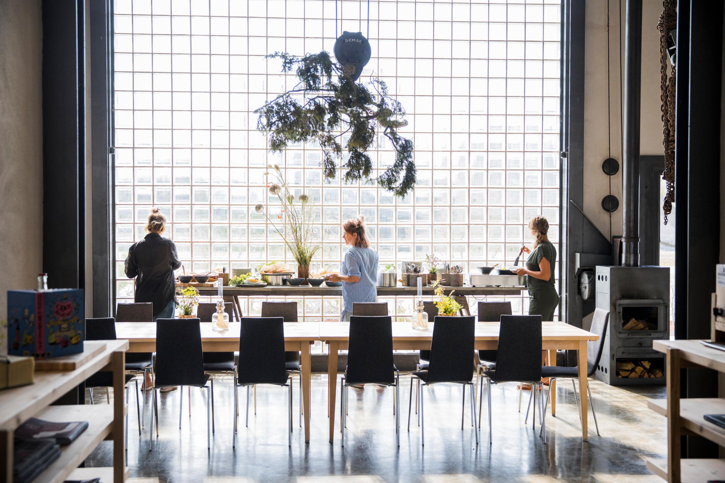 A buffet in front of a large window at a restaurant. Three persons pick food from the buffet.