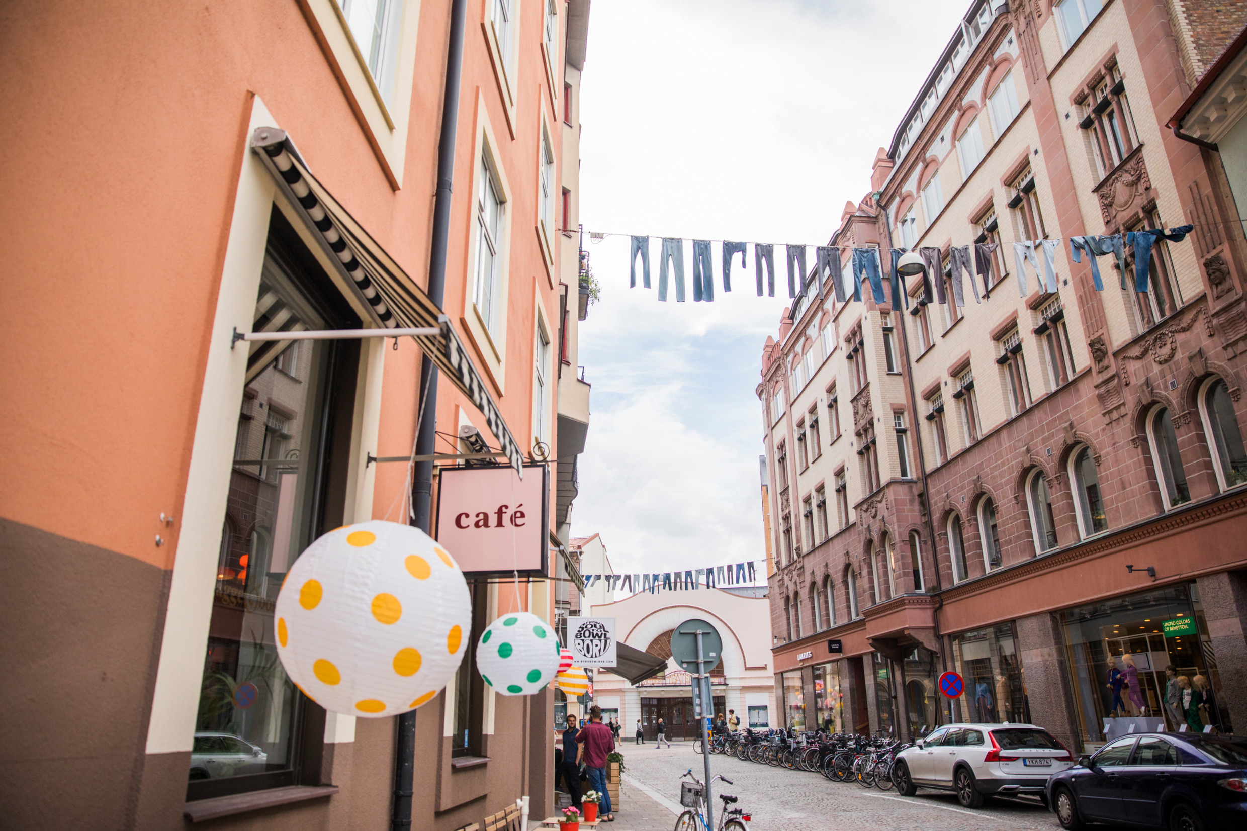Eine Straße mit Steinhäusern auf jeder Seite. Hosen hängen auf der Wäscheleine auf der anderen Straßenseite. Mehrere Fahrräder und zwei Autos sind entlang der Straße geparkt.