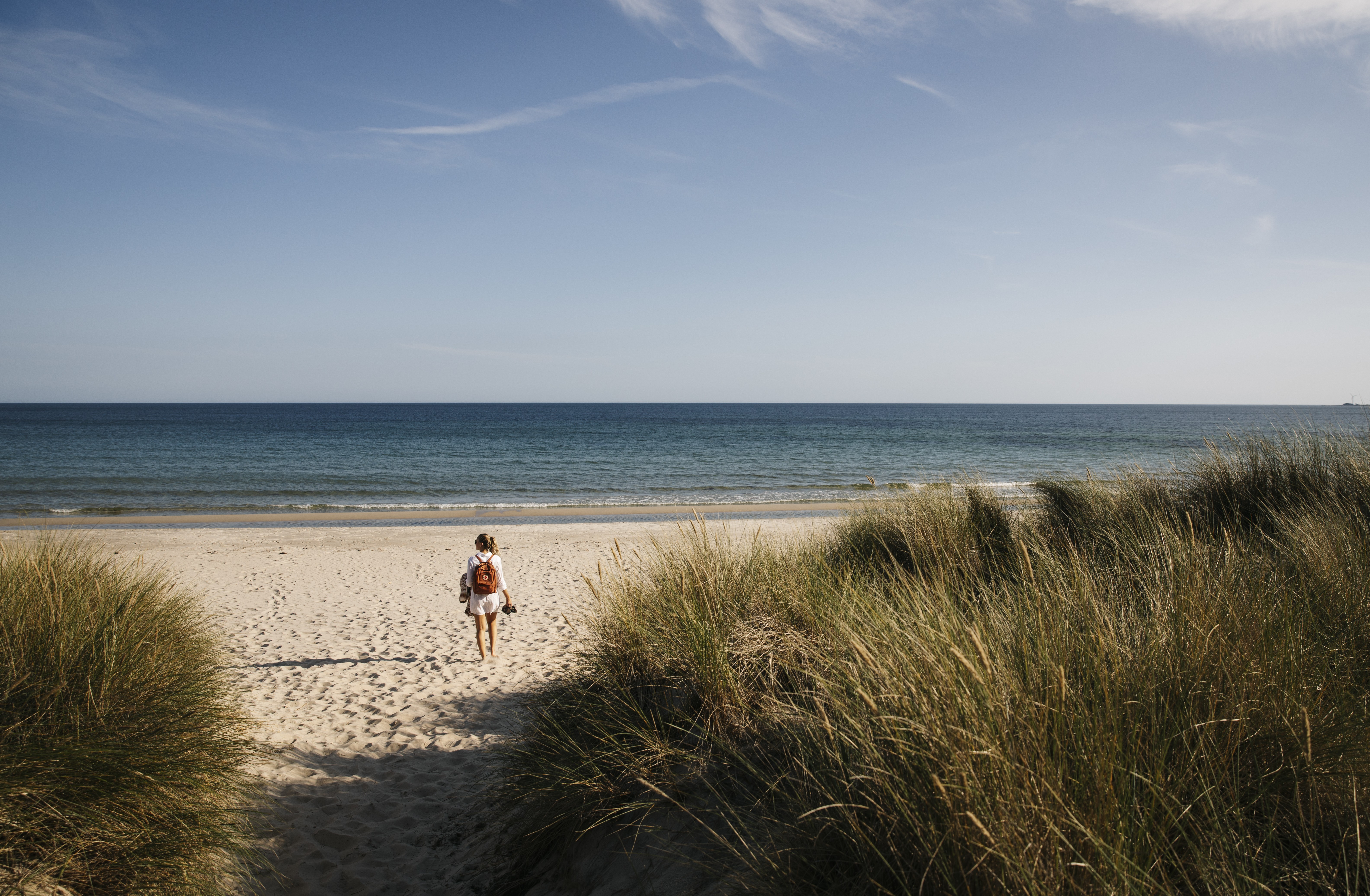A woman walking on a beautiful beach with the sea and a blue sky in the background.