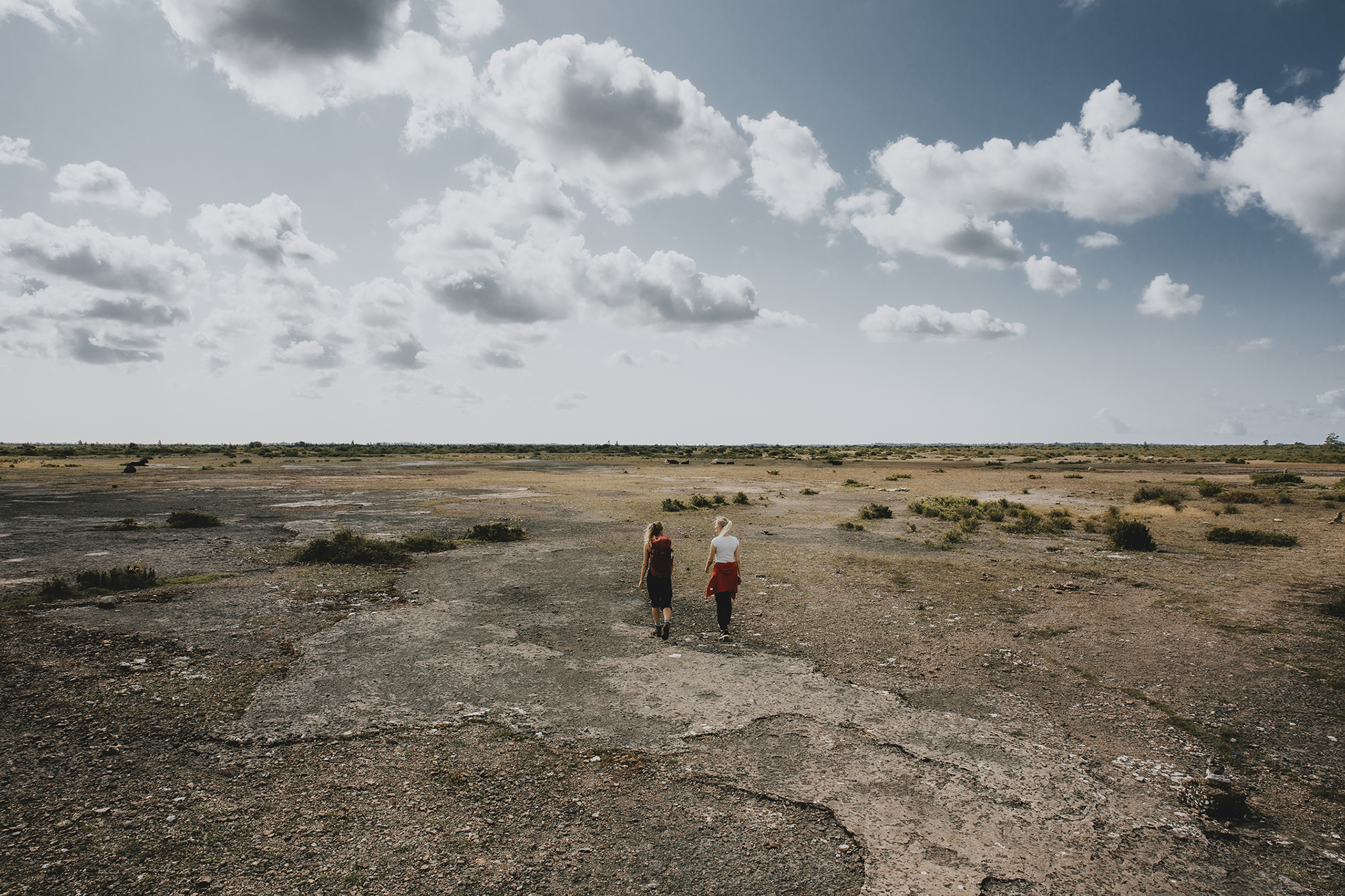 Two people walking across a flat, open limestone plain with sparse vegetation under a wide sky on Öland.