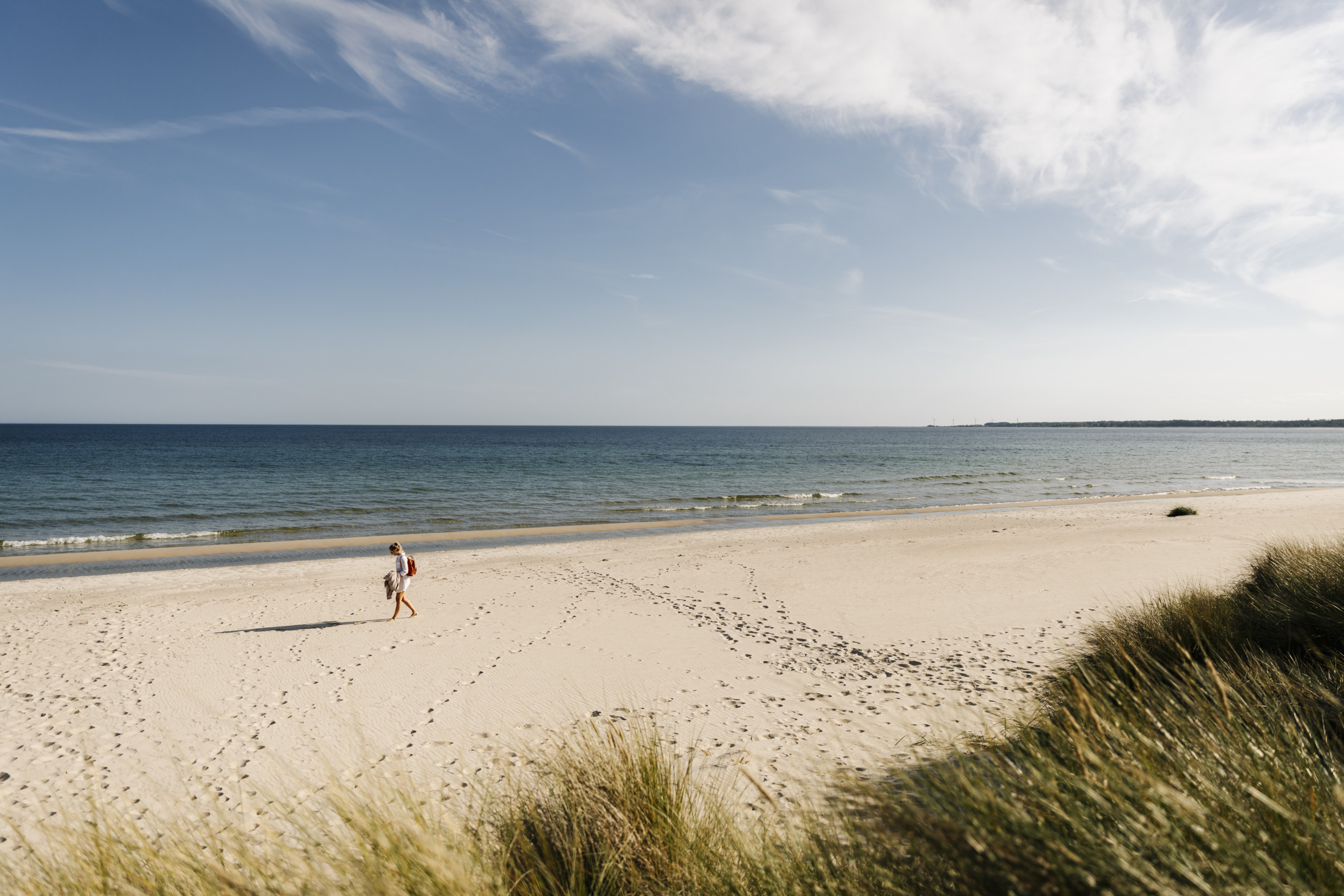 Une femme en train de marcher sur une magnifique plage avec la mer et le ciel bleu en arrière-plan.