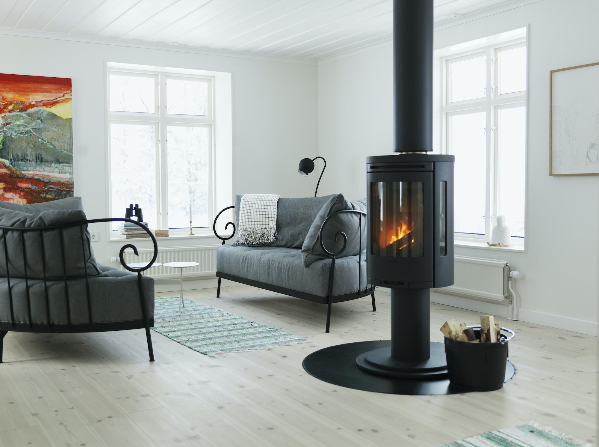 Ein Wohnzimmer mit zwei Sofas und einem Kamin. Zwei Gemälde hängen an einer weißen Wand neben den Fenstern.