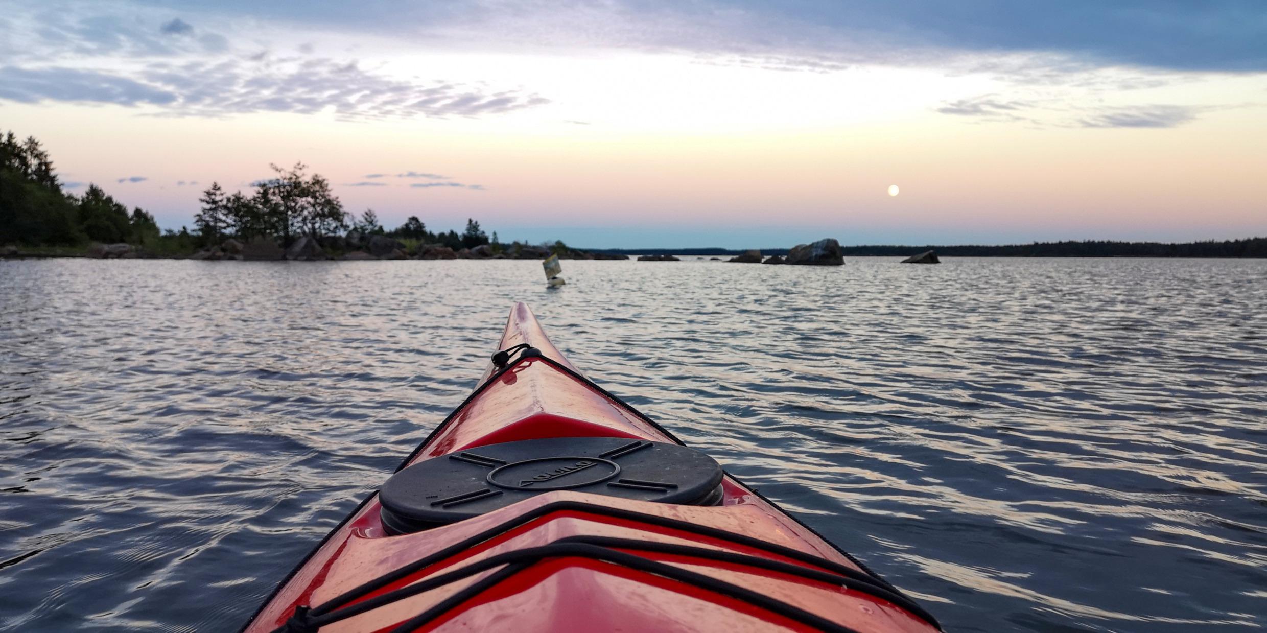 Der vordere Teil eines roten Kanus auf dem Wasser im Archipel. Die Sonne geht unter.