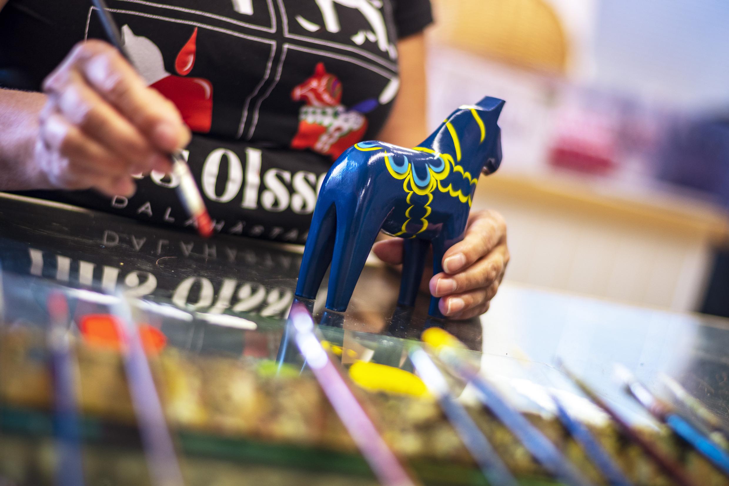 Someone painting a pattern on a blue Dala horse.