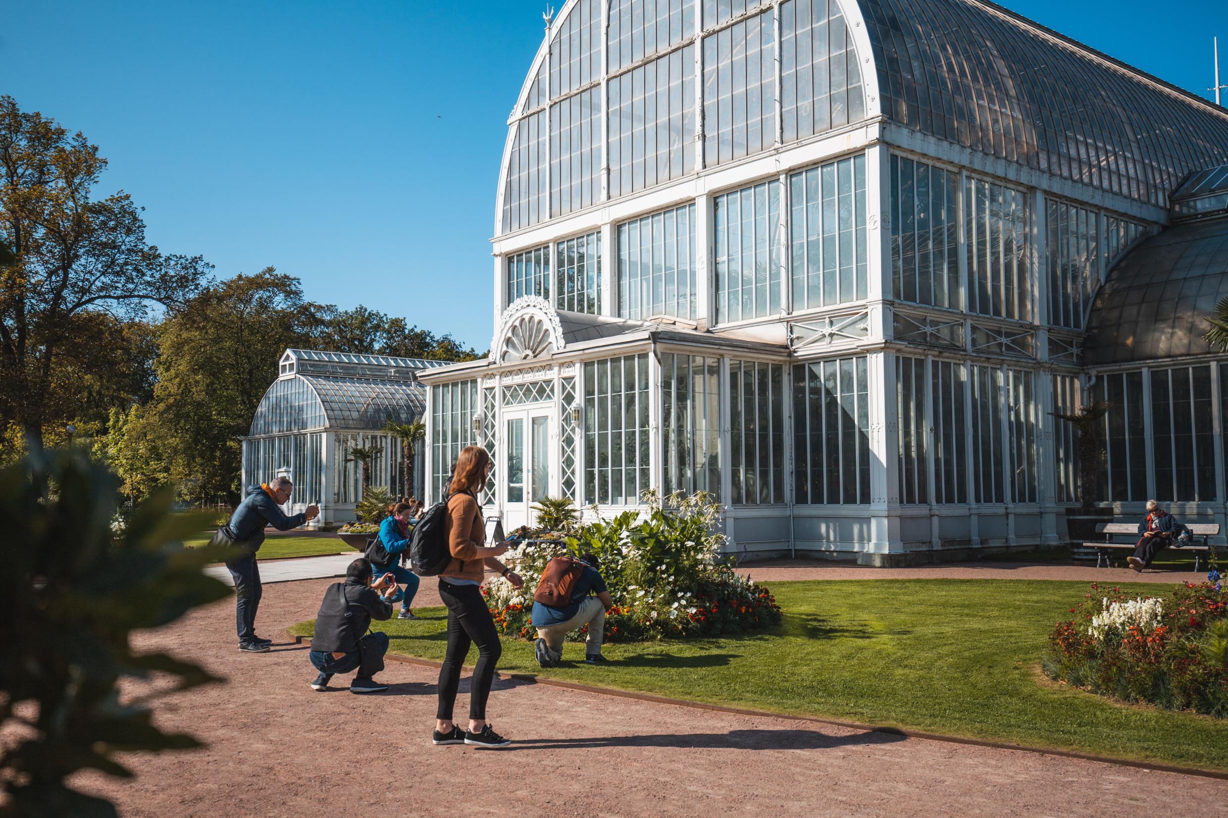 Vijf personen die foto's maken van een bloemperk buiten een grote kas, het Palmhuis.