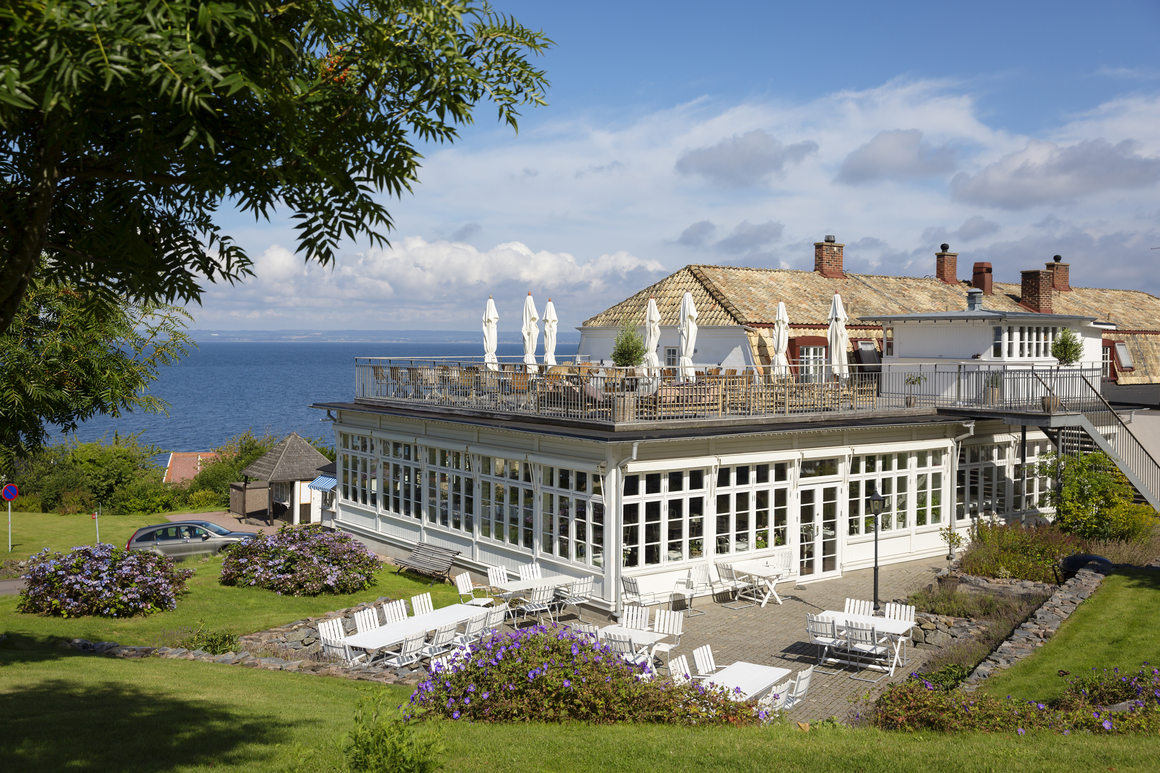 Rusthållargården in Arild, met een groot terras, wit tuinmeubilair en bloembedden met uitzicht op zee.