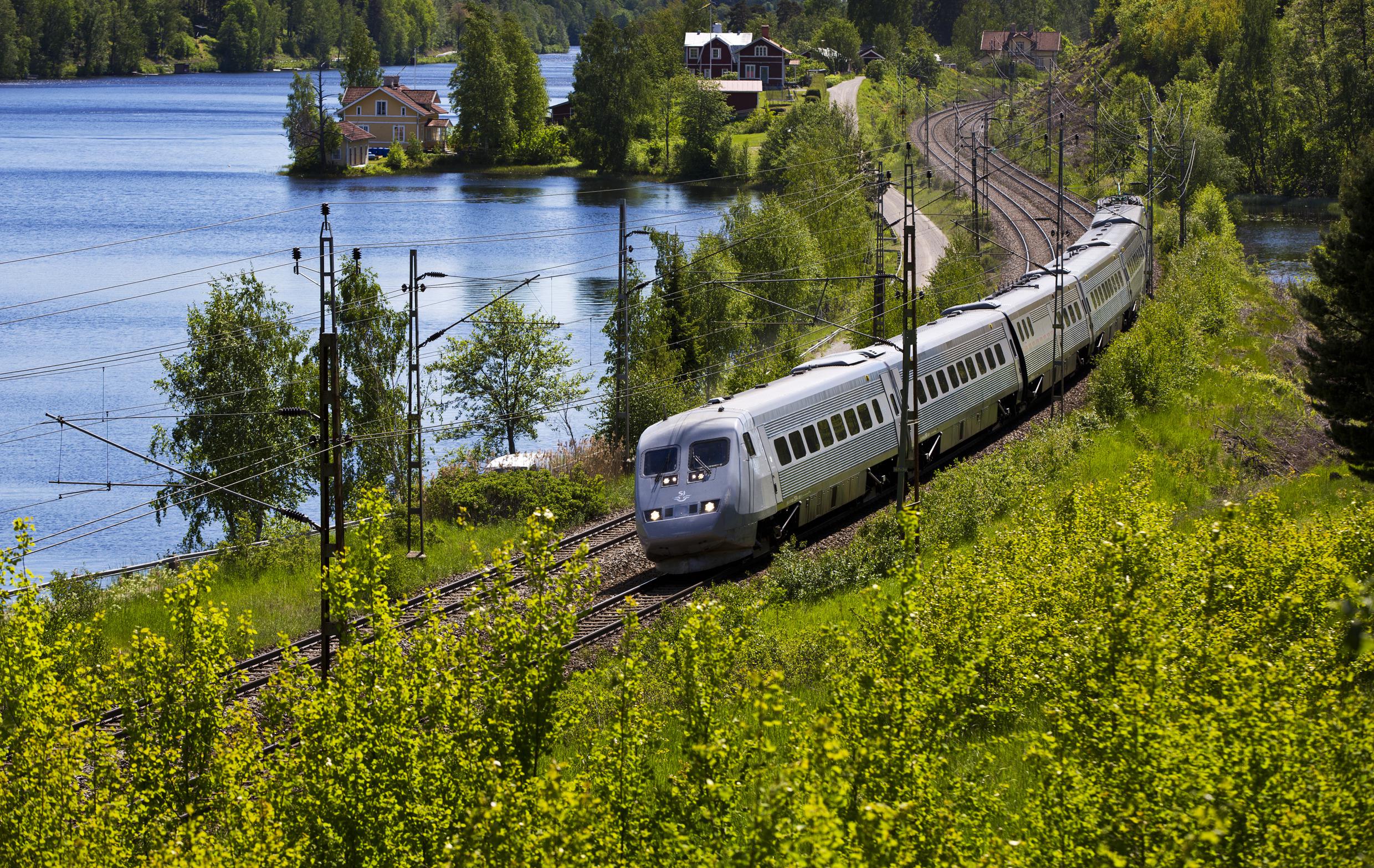 Een trein die in de zomer langs een meer rijdt.