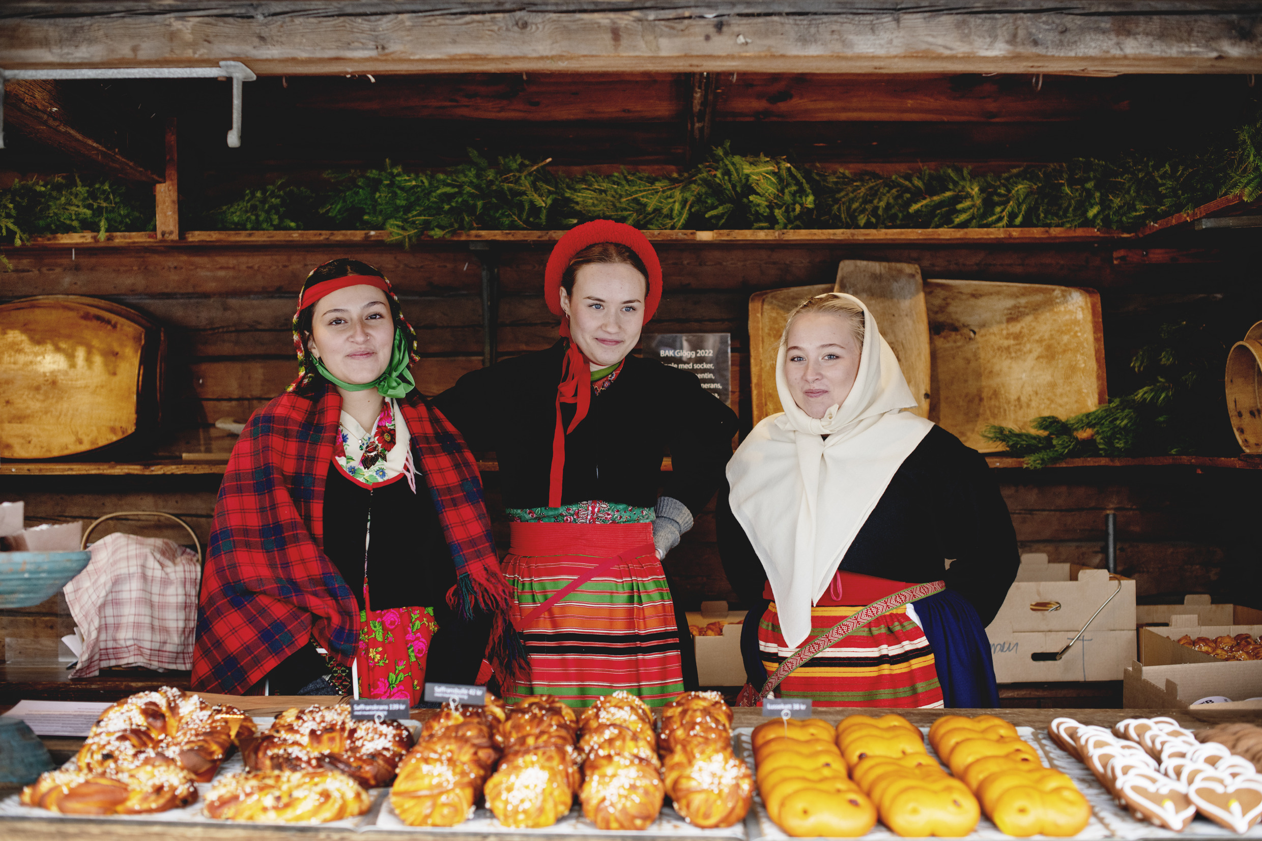 Trois femmes en tenue traditionnelle vendent des brioches au safran (« lussekatter ») et des pâtisseries au marché de Noël de Skansen.
