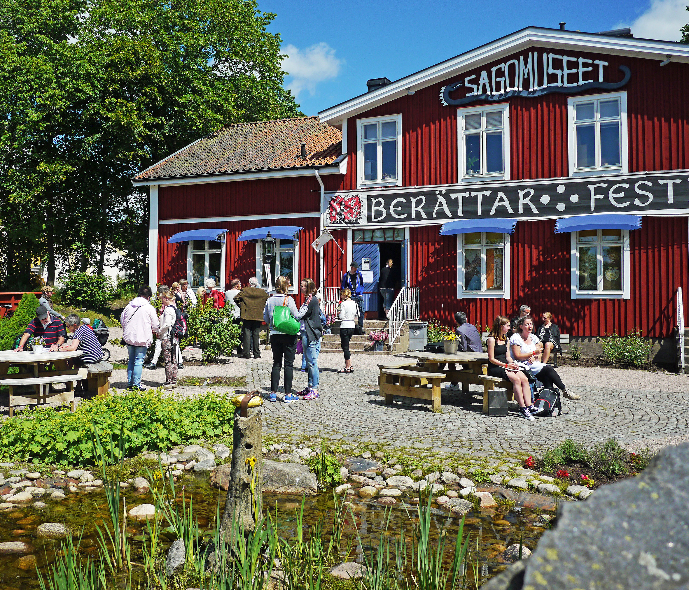 Des visiteurs se trouvent devant le bâtiment rouge en bois du Musée des légendes à Ljungby, en Suède. Ce musée fait partie de la région narrative « Le pays des légendes ».