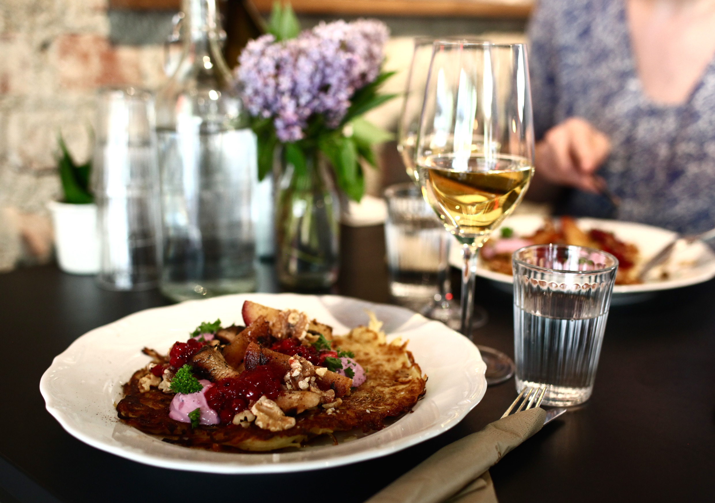 Auf einem Teller mit Rösti, gebratenen Äpfeln, Preiselbeeren und Kräutern, serviert im Jazzkökets Saluhall in Östersund, mit einem Weinglas und Wasser auf einem gedeckten Tisch.