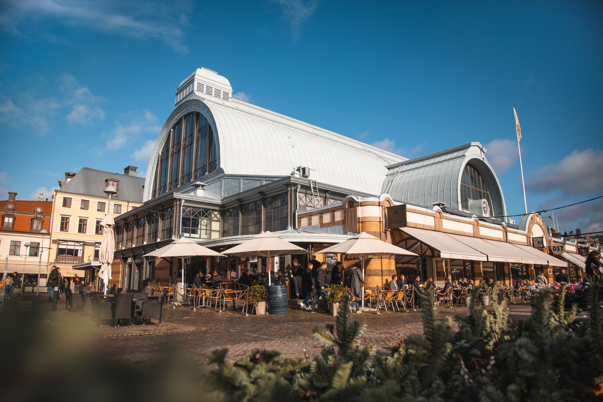 Vue extérieure de Stora Saluhallen à Göteborg, une grande halle historique où l'on peut s'asseoir en plein air et déguster des plats sous de grands parasols.