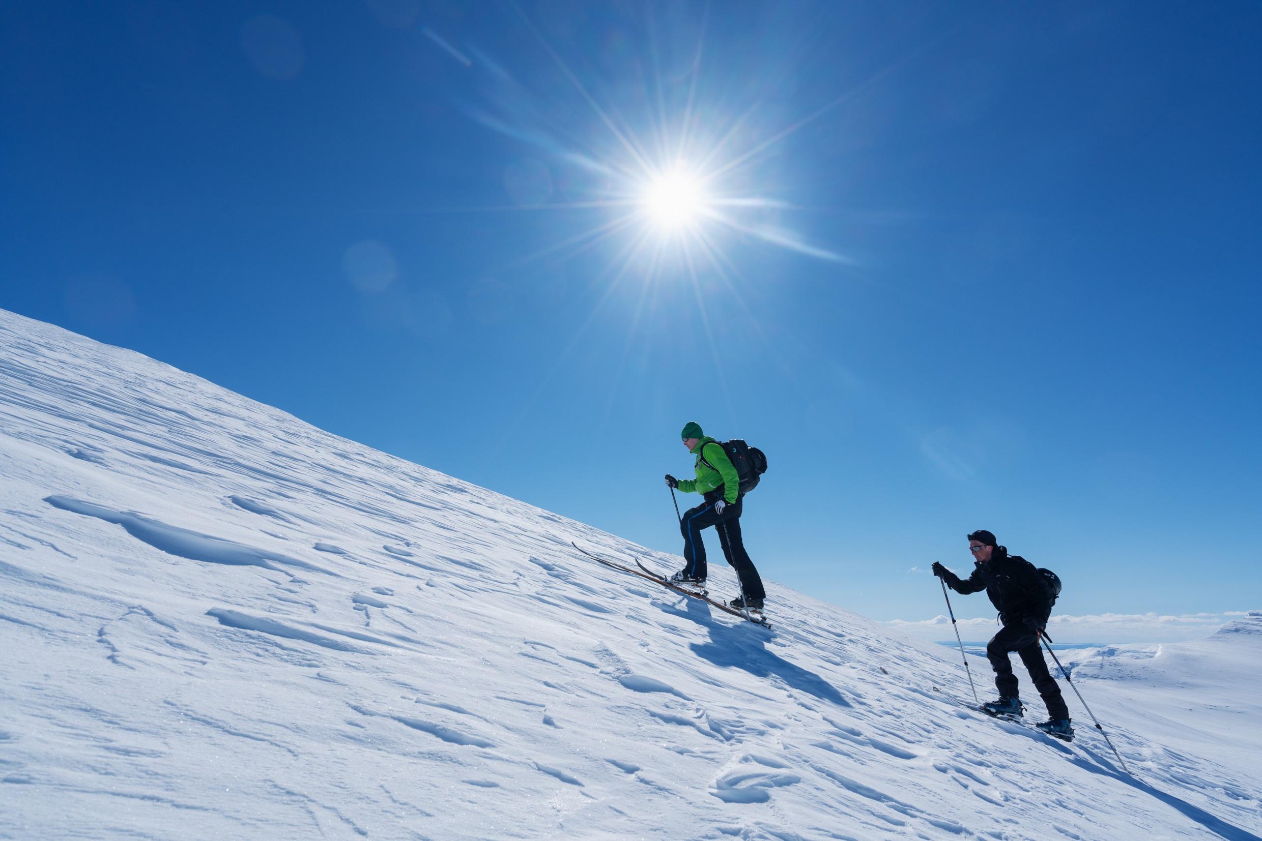 Deux personnes avec des skis gravissent une pente enneigée.