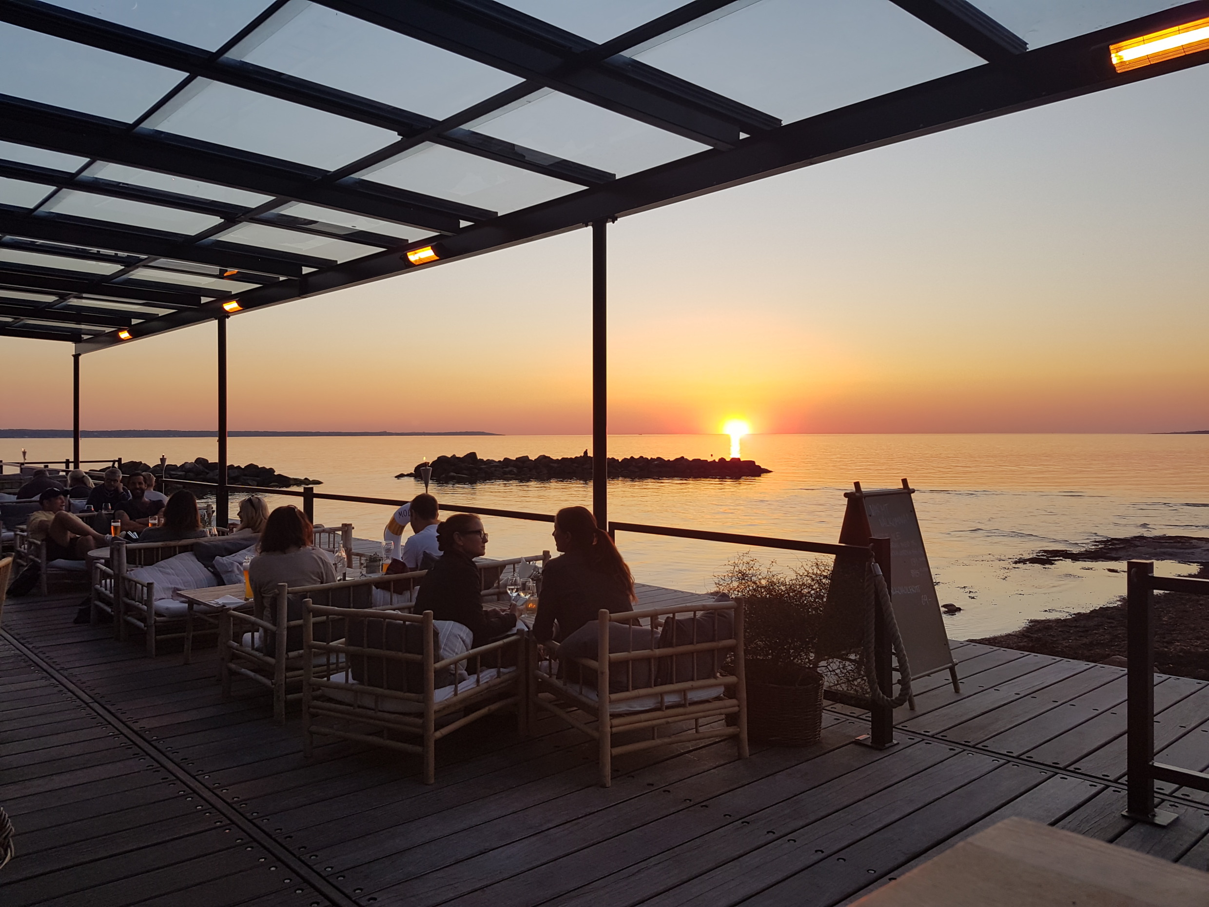 Gäste genießen Meeresfrüchte auf der Terrasse des Sillen & Makrillen mit Blick auf den Sonnenuntergang über der Meerenge Öresund in Helsingborg.