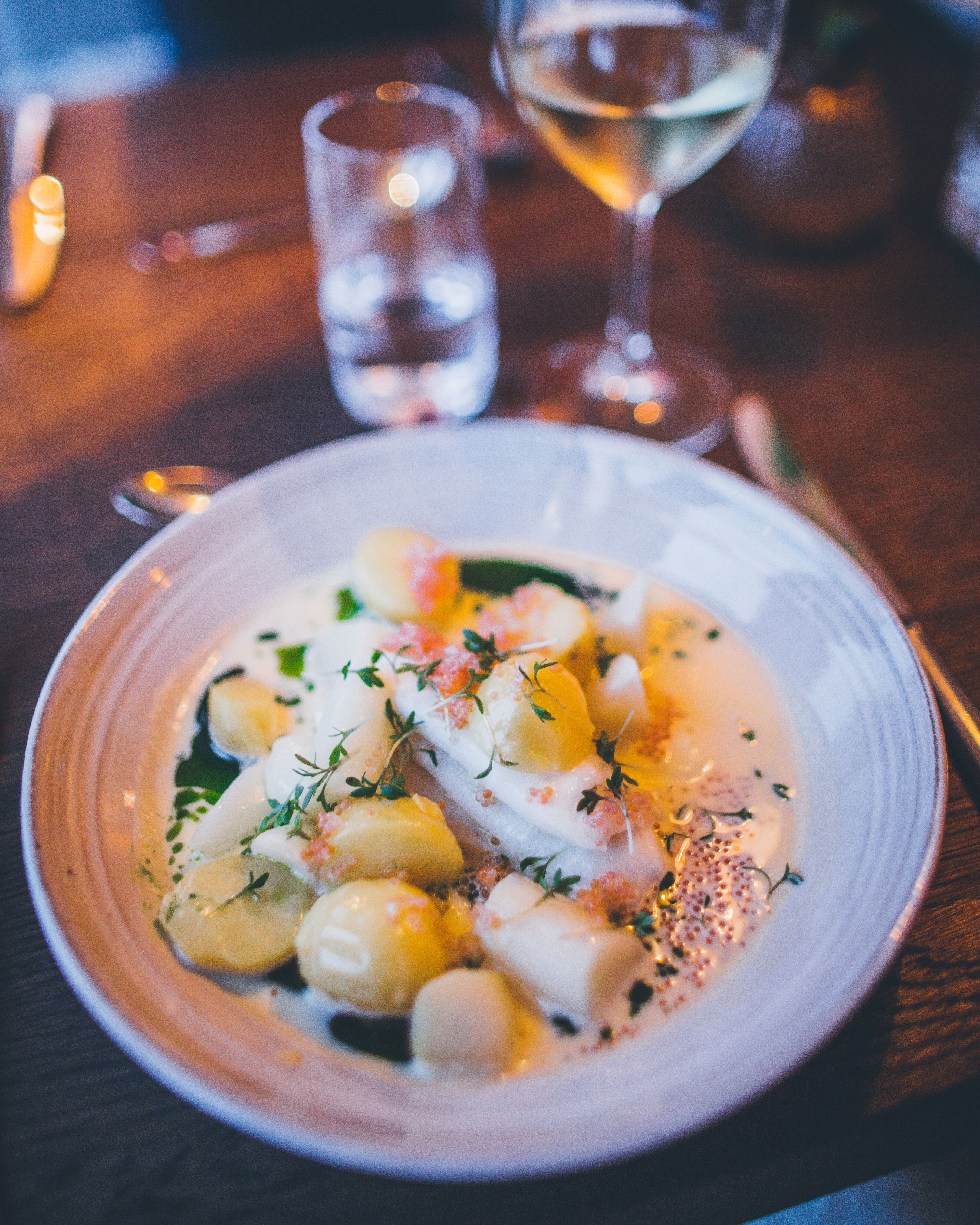 Een visgerecht dat bij Skärets Krog in een witte kom wordt geserveerd, met een glas witte wijn op een restauranttafel.