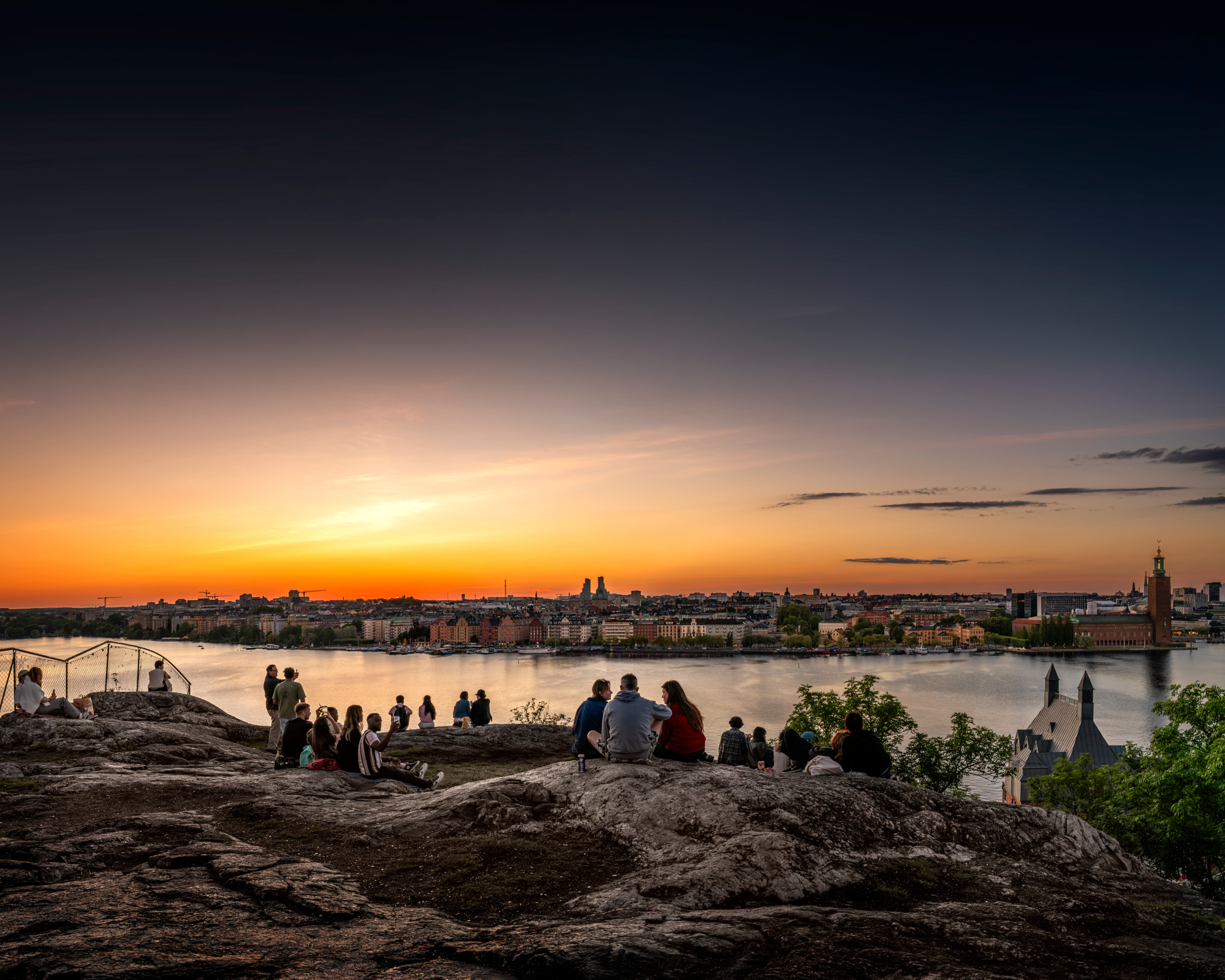 Des personnes assises et debout sur une falaise surplombant l'eau et une ville.