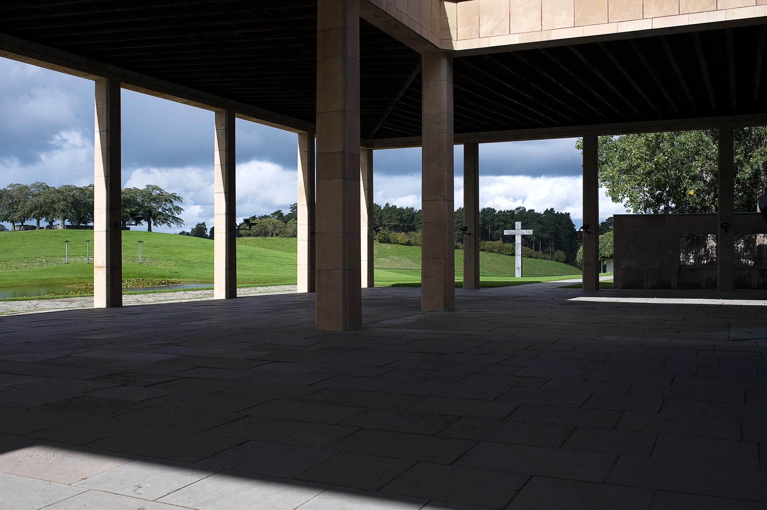 Das Gebäude des Woodland-Friedhofs mit den sichtbaren Säulen. Hinter den Säulen befindet sich ein Kreuz und im Hintergrund sind Hügel und Bäume zu sehen.