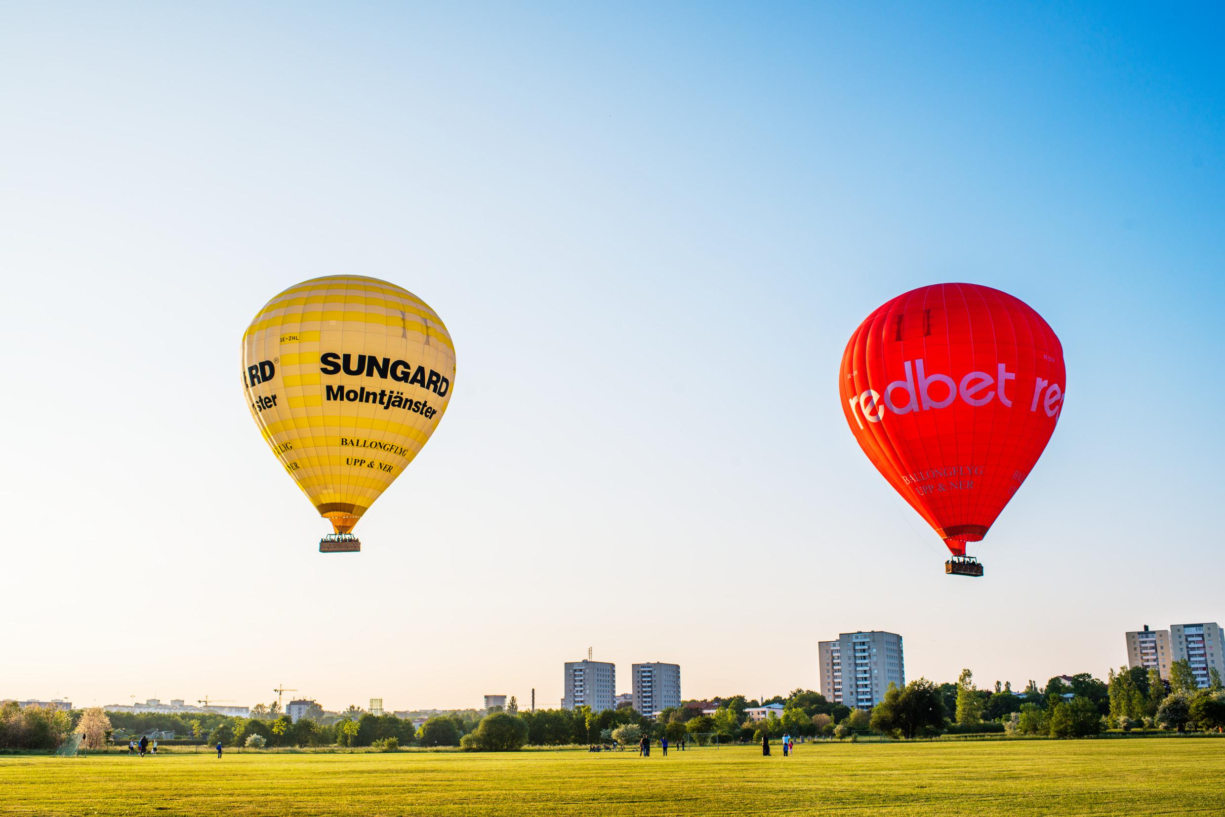 Hot air balloons gliding across the Stockholm skyline, over a park, high-rises in the background.