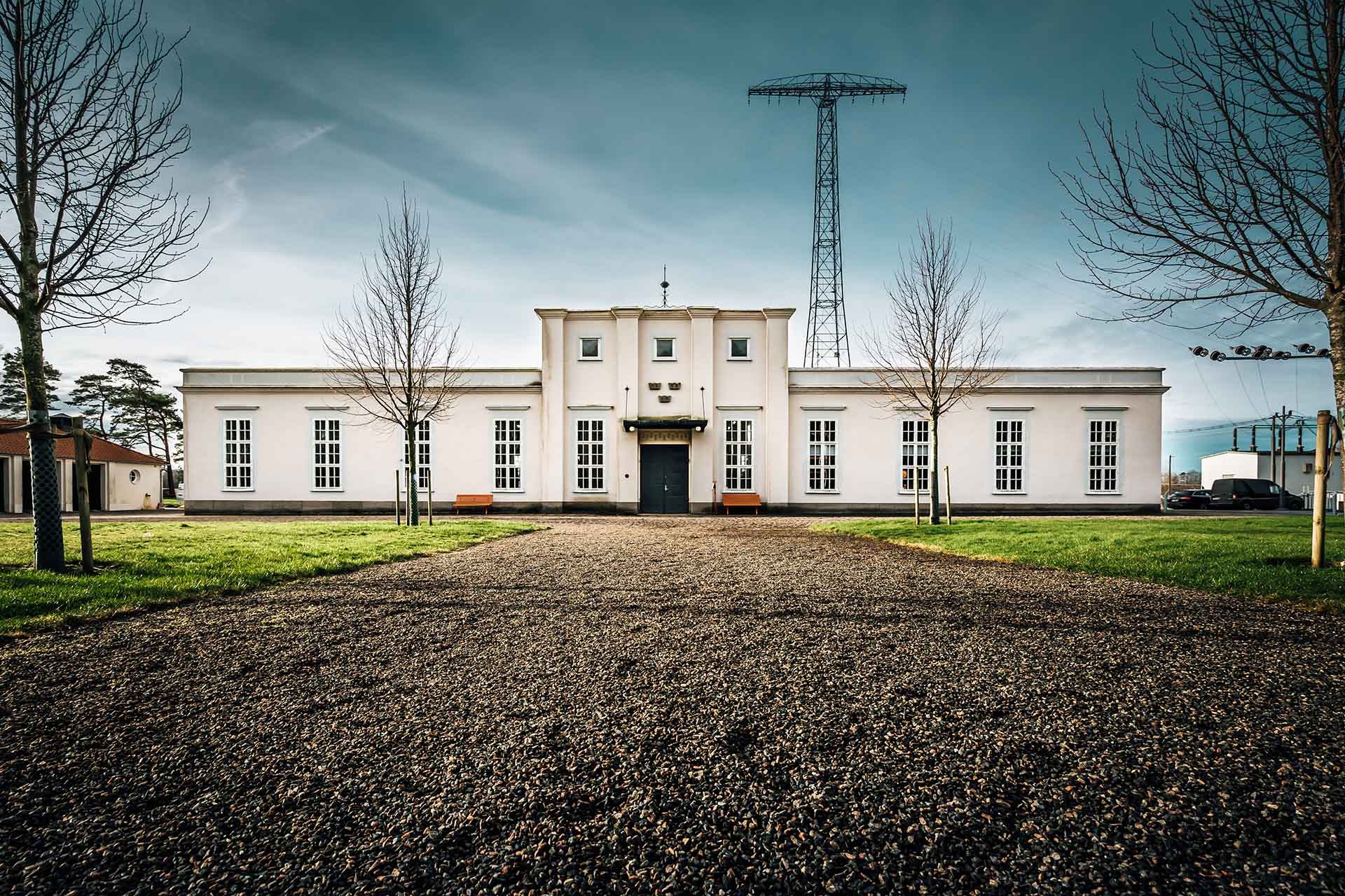 A child is playing in a park in front of a white stone house with a transmitter mast.
