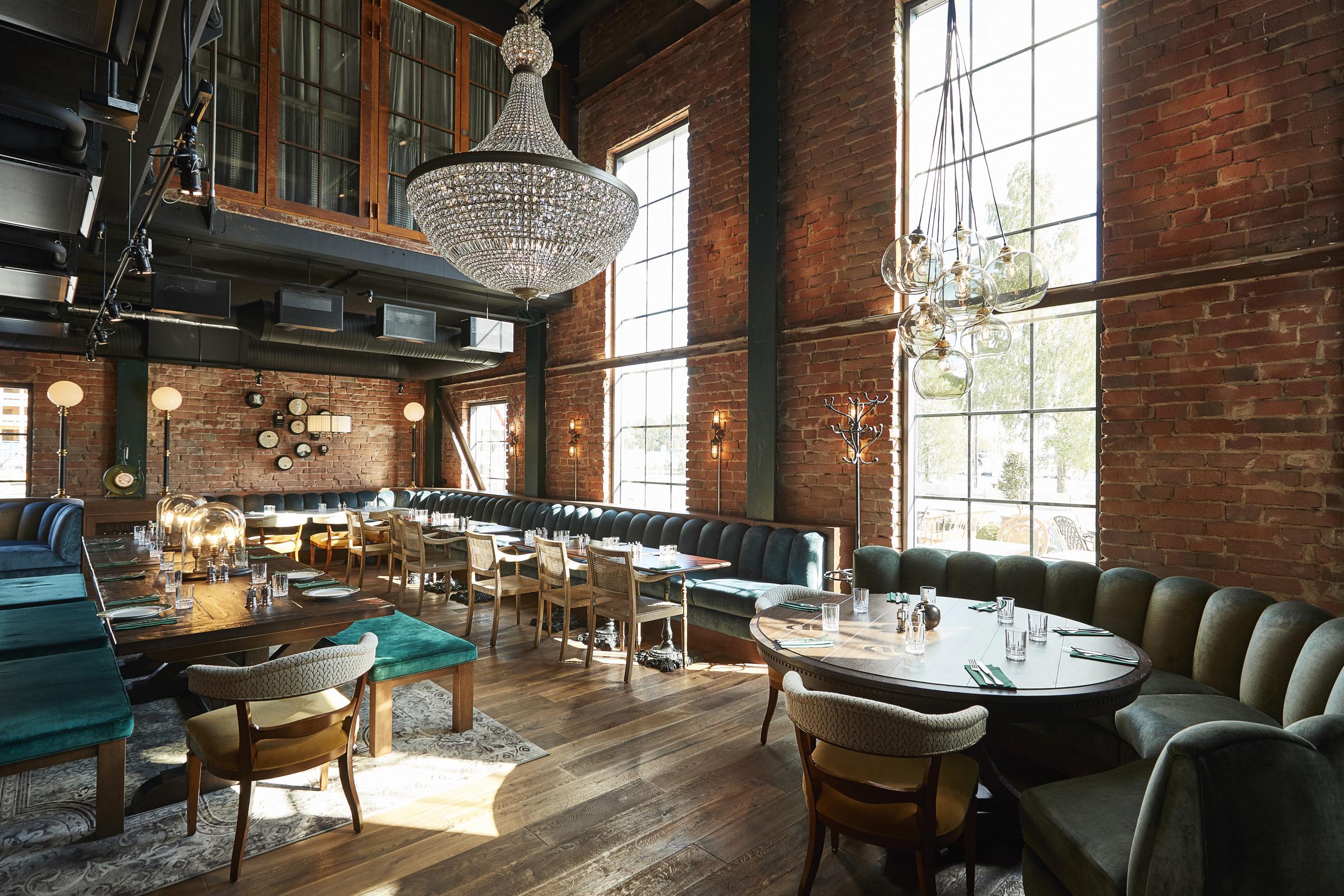 L'intérieur du Steam Hotel, avec des murs en briques, des canapés en velours turquoise et des meubles en bois. Un lustre au premier plan. Des murs avec de grandes fenêtres.