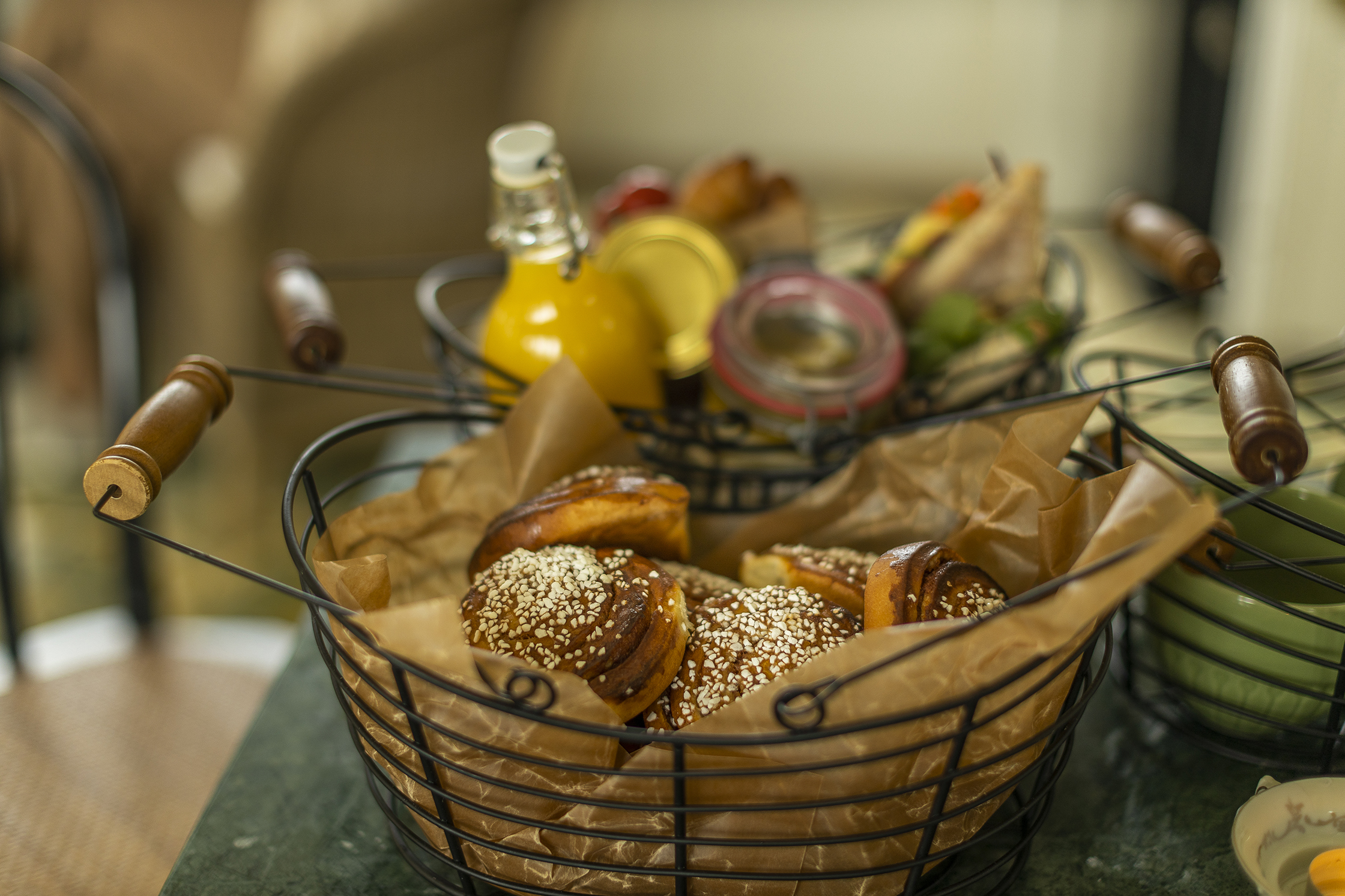 Een mand met kaneelbroodjes op een tafel, naast sap en ontbijtproducten in de ontbijtzaal van een hotel.
