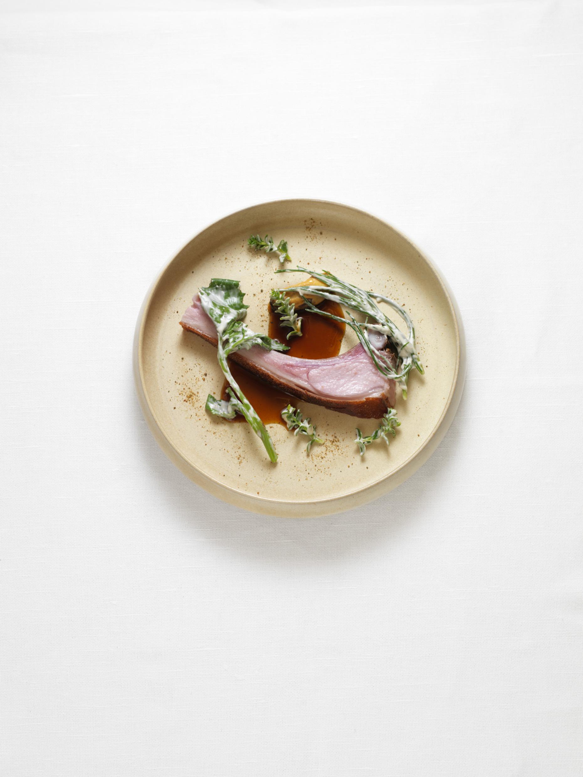 Close-up on a dish with suckling pig from Västerslät with maritime weeds and mussels.