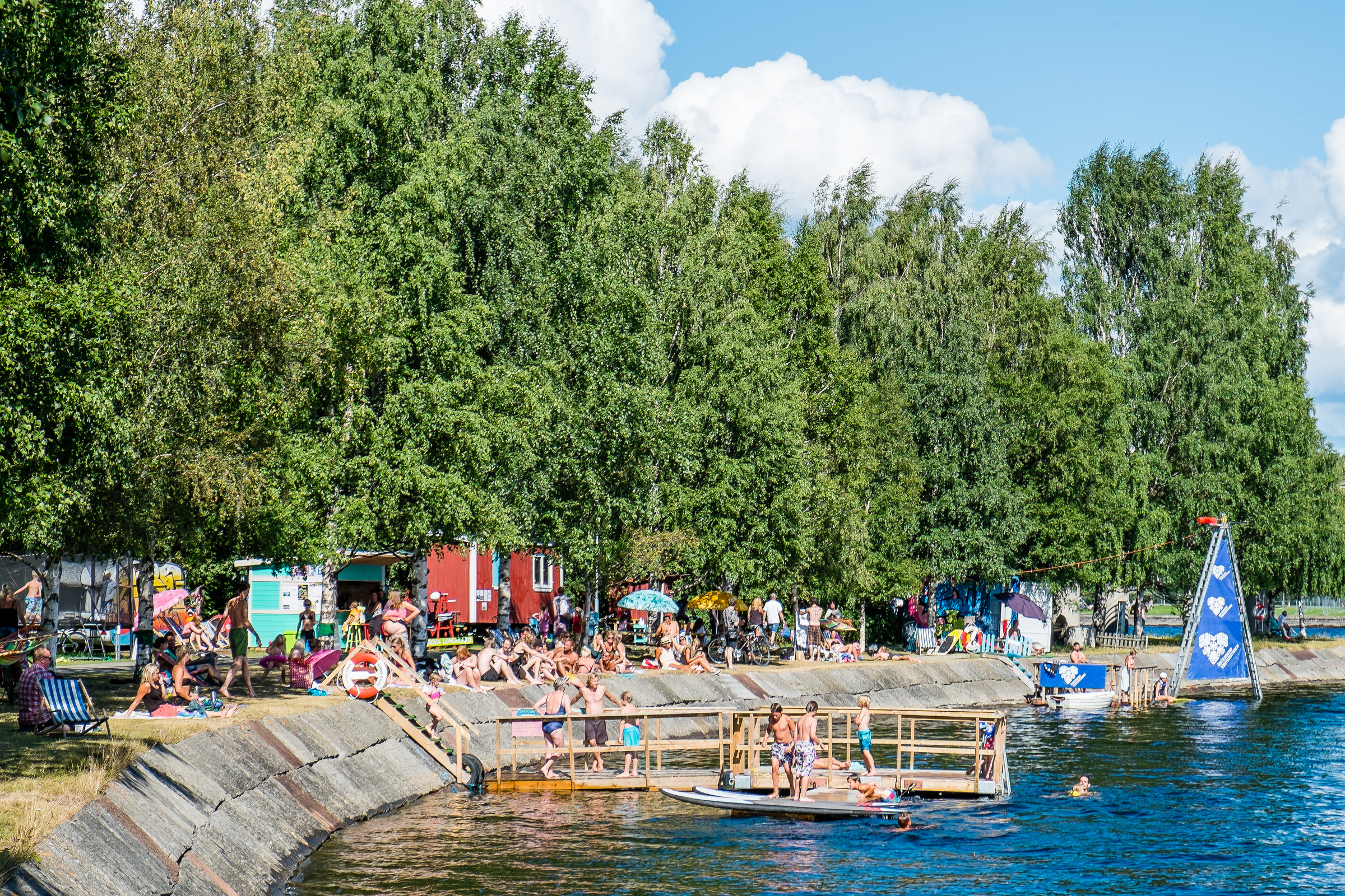 Leute, die Sommeraktivitäten wie Schwimmen und Chillen am Wasser in Surfbukten in Östersund genießen, umgeben von üppig grünen Bäumen.