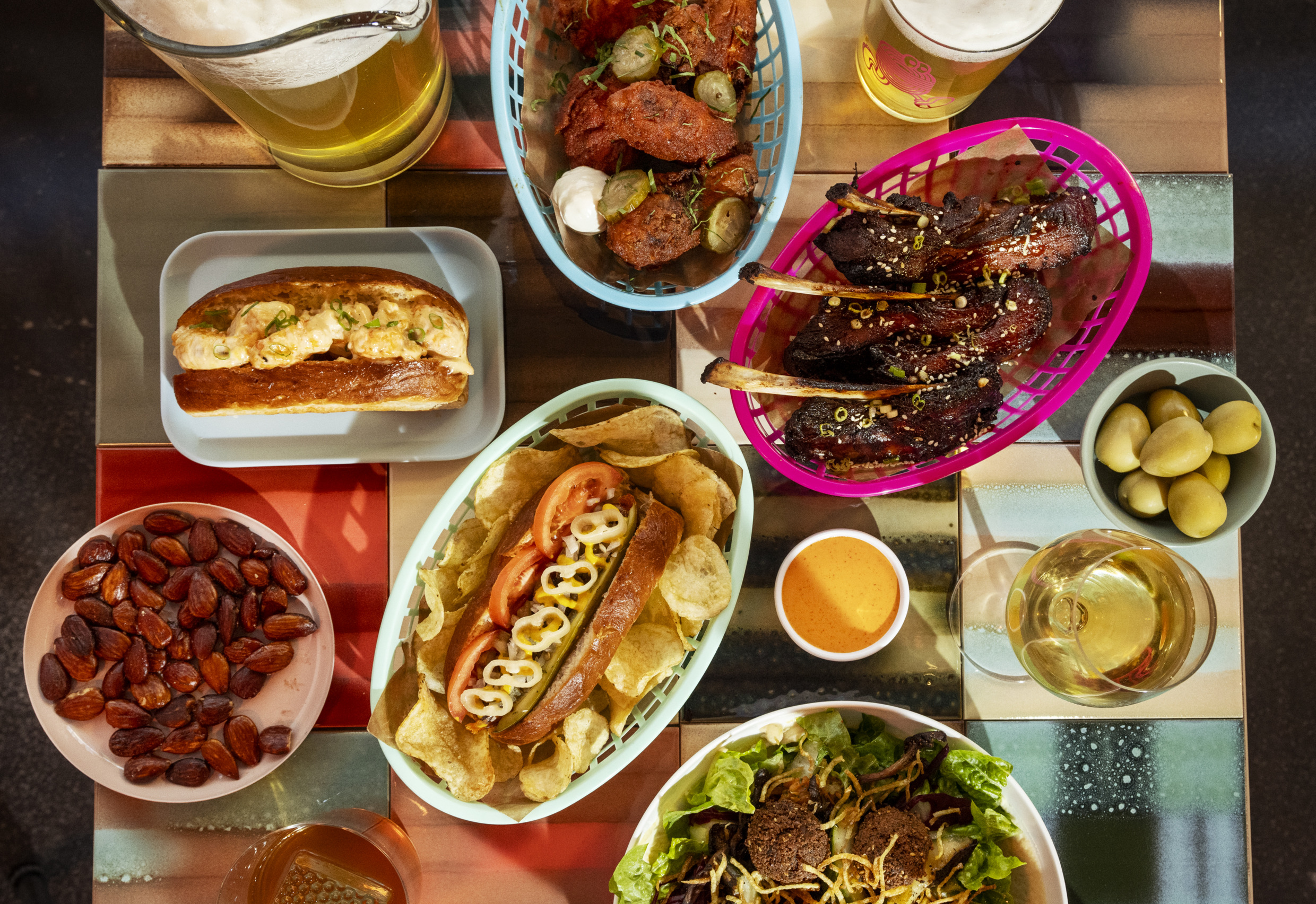 Ein quadratischer Tisch, gefüllt mit buntem Streetfood in verschiedenen Körben und auf Tellern, sowie Gläsern mit Bier und Wein.